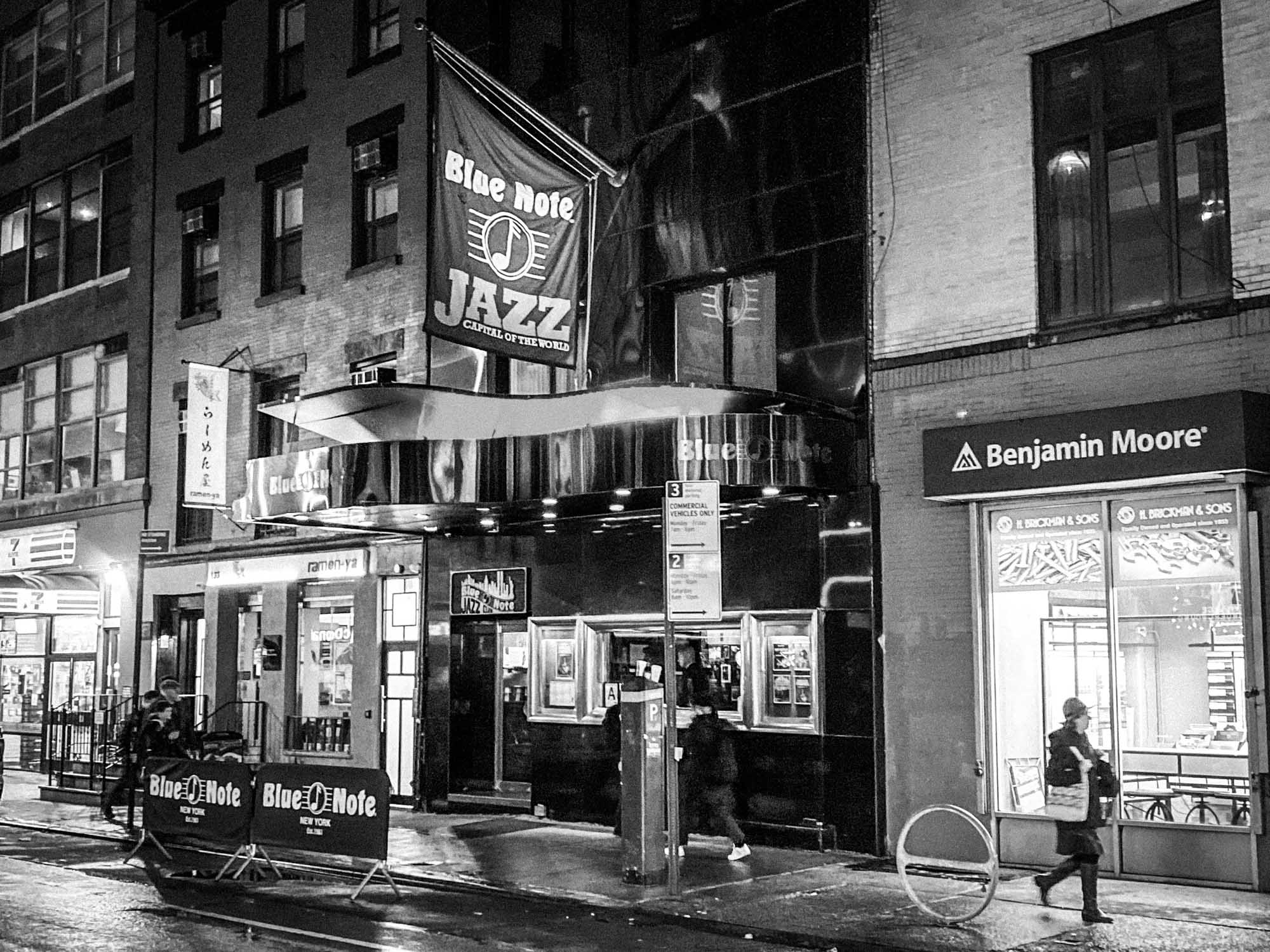 Exterior of Blue Note Jazz Club in New York City at night, with a lit Benjamin Moore store nearby.