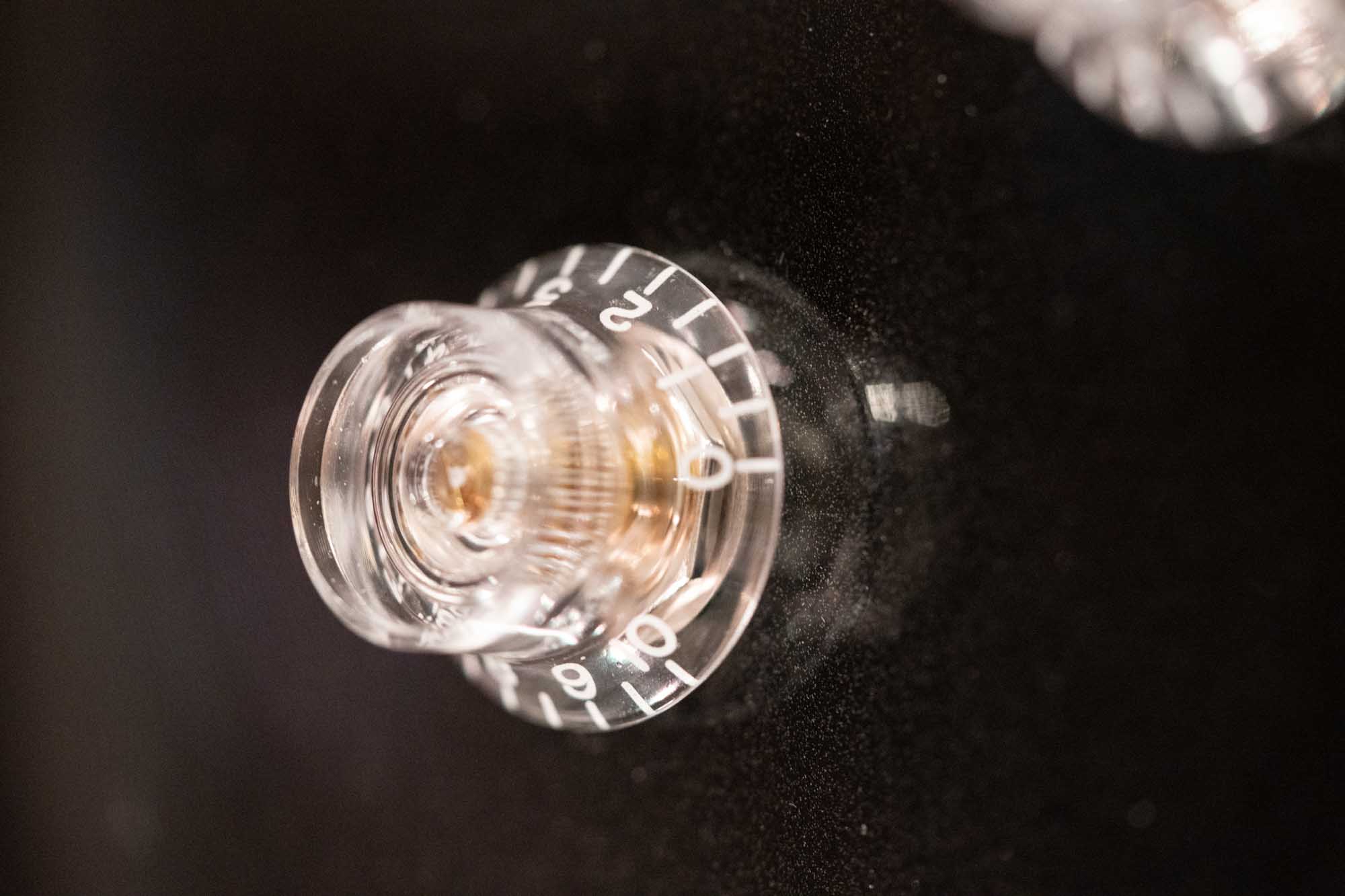 Close-up of a clear guitar volume knob with numbered dial on a black surface.