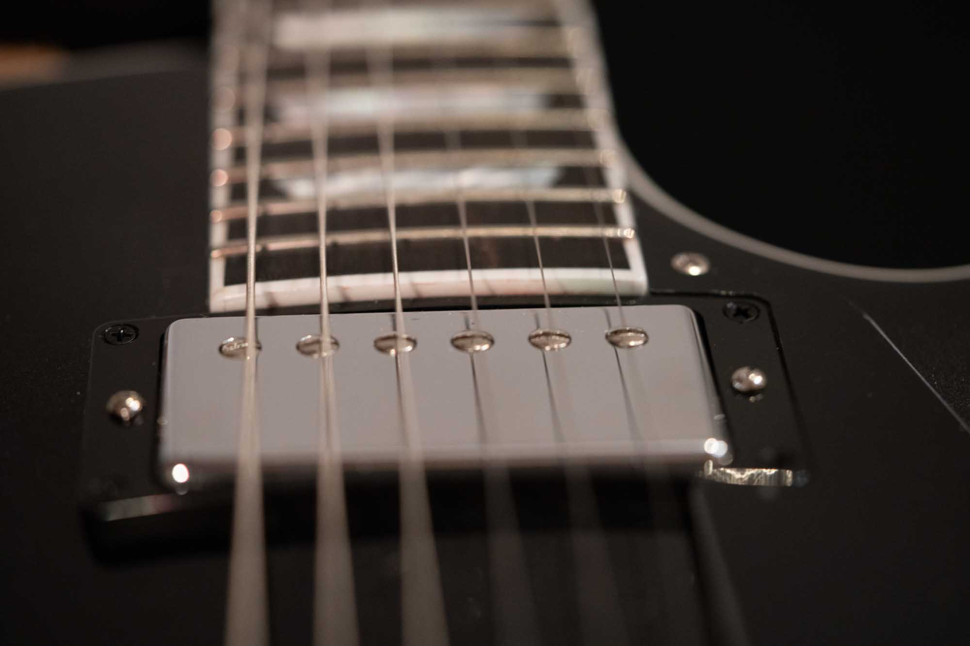 Close-up of an electric guitar's strings and pickups, highlighting the metallic details and black finish.