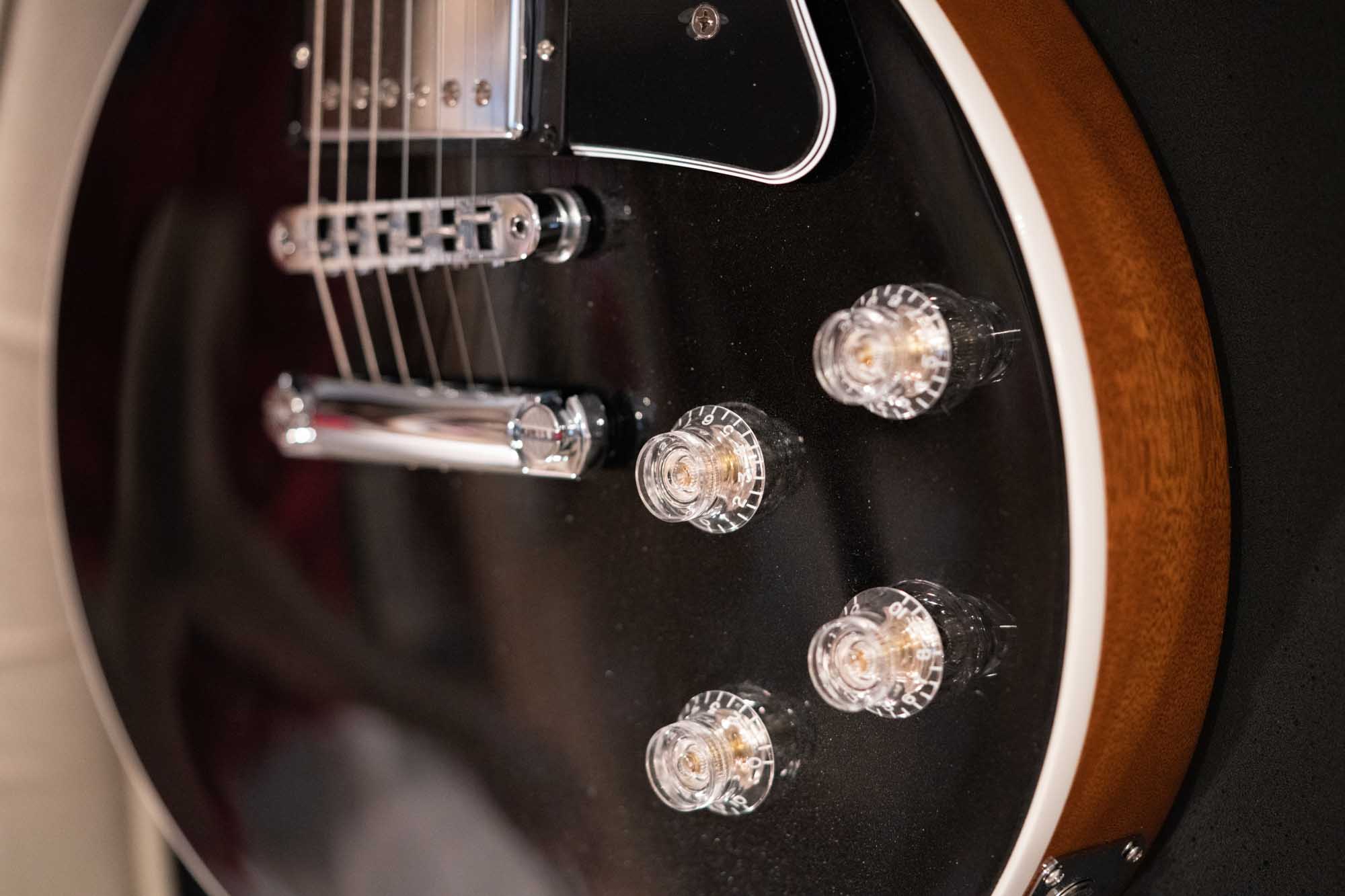 Close-up of a black electric guitar body with strings and control knobs visible.