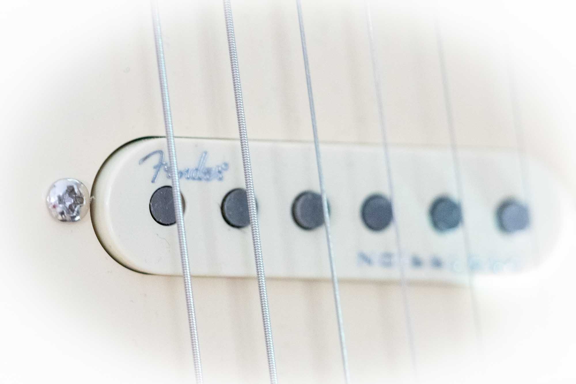 Close-up of an electric guitar pickup with metal strings, featuring the word Fender on the cream housing.