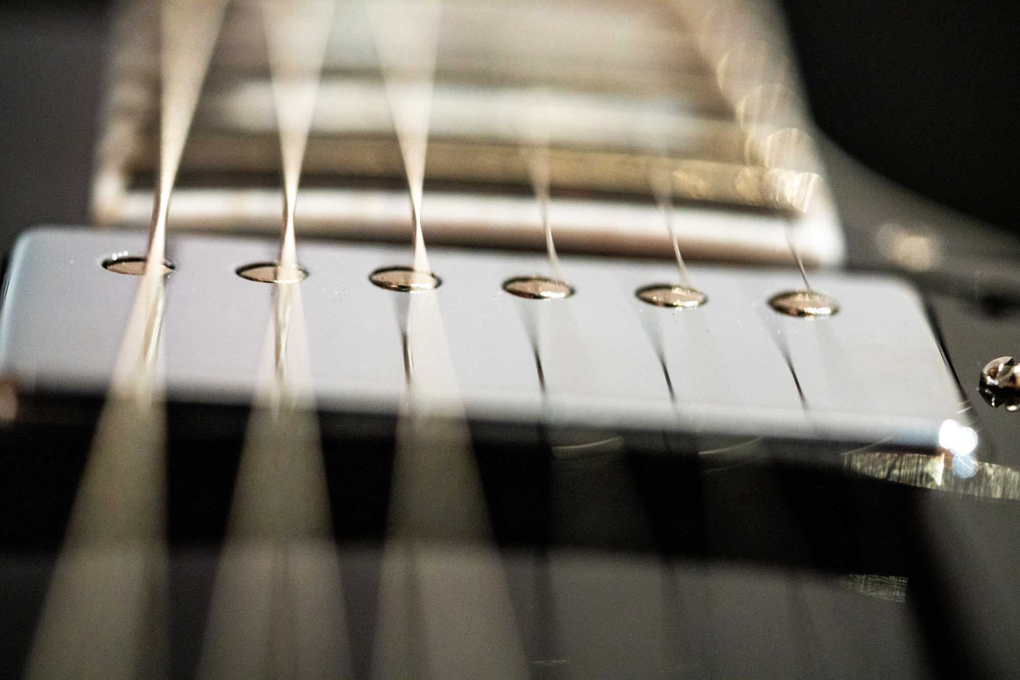 Close-up of electric guitar strings and pickup, capturing their polished, metallic shine.