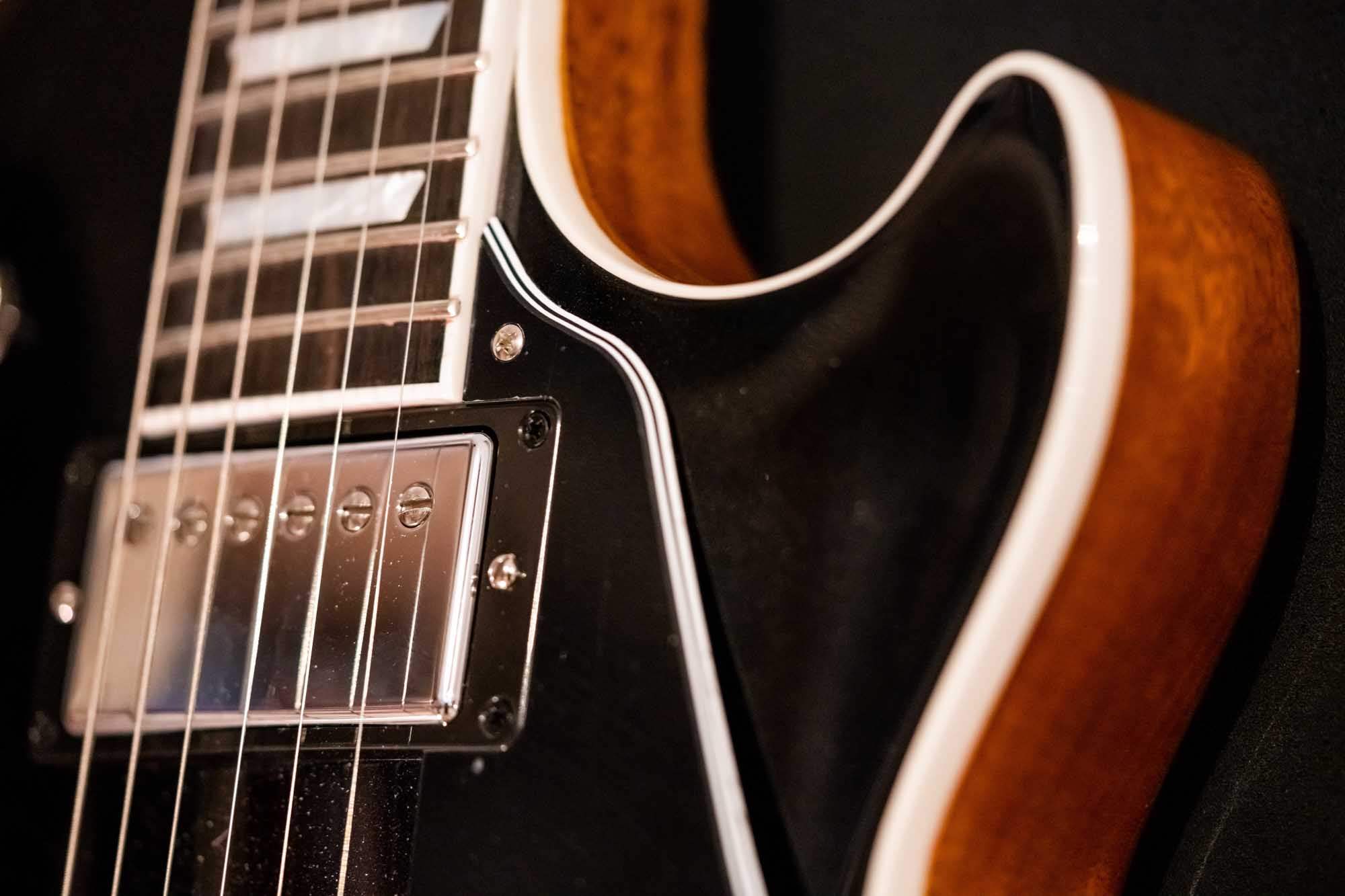 Close-up of an electric guitar body, highlighting strings and brown wood finish against a dark background.