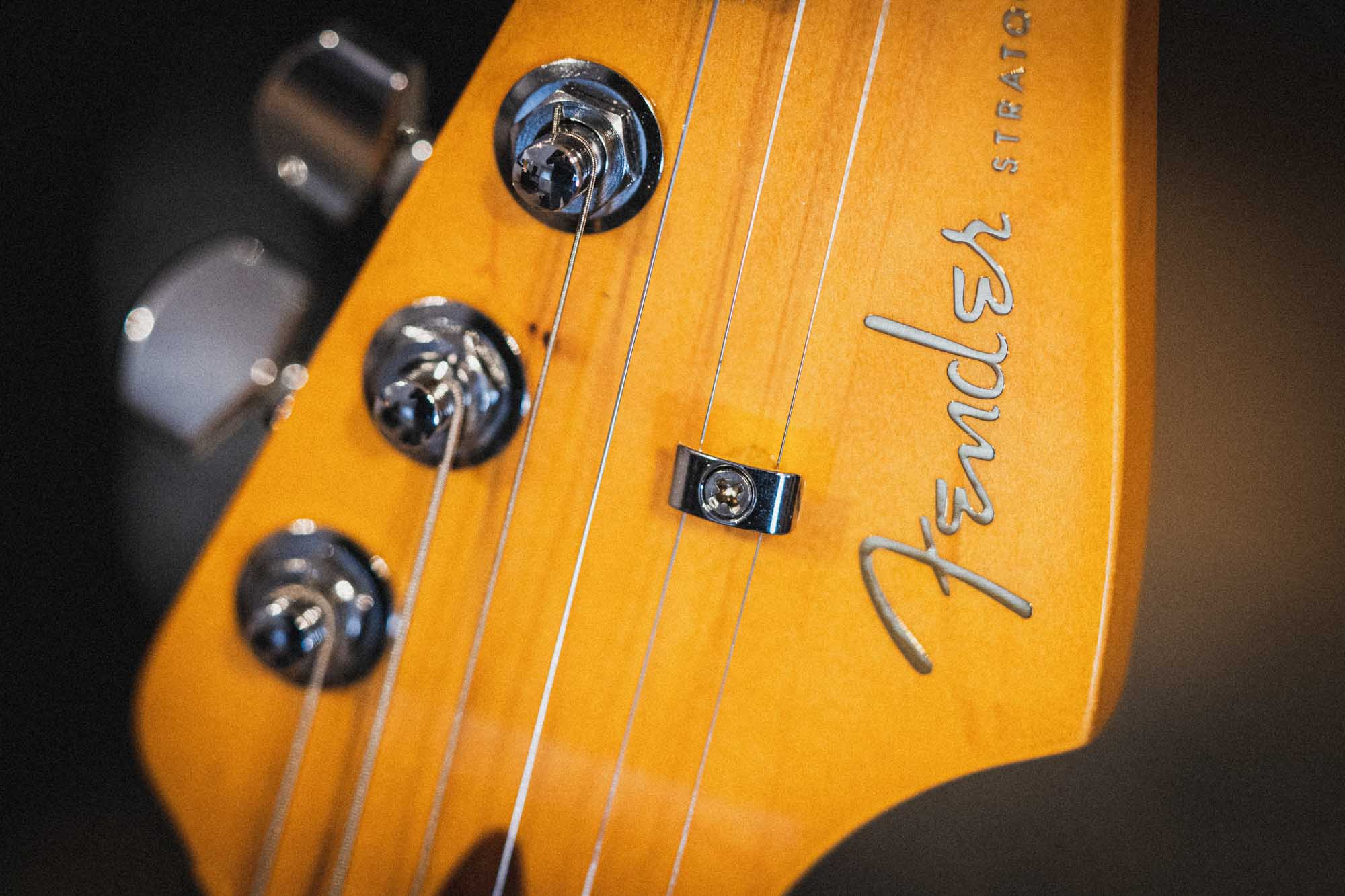 Close-up of Fender Stratocaster headstock with tuning pegs and logo on a wooden finish.