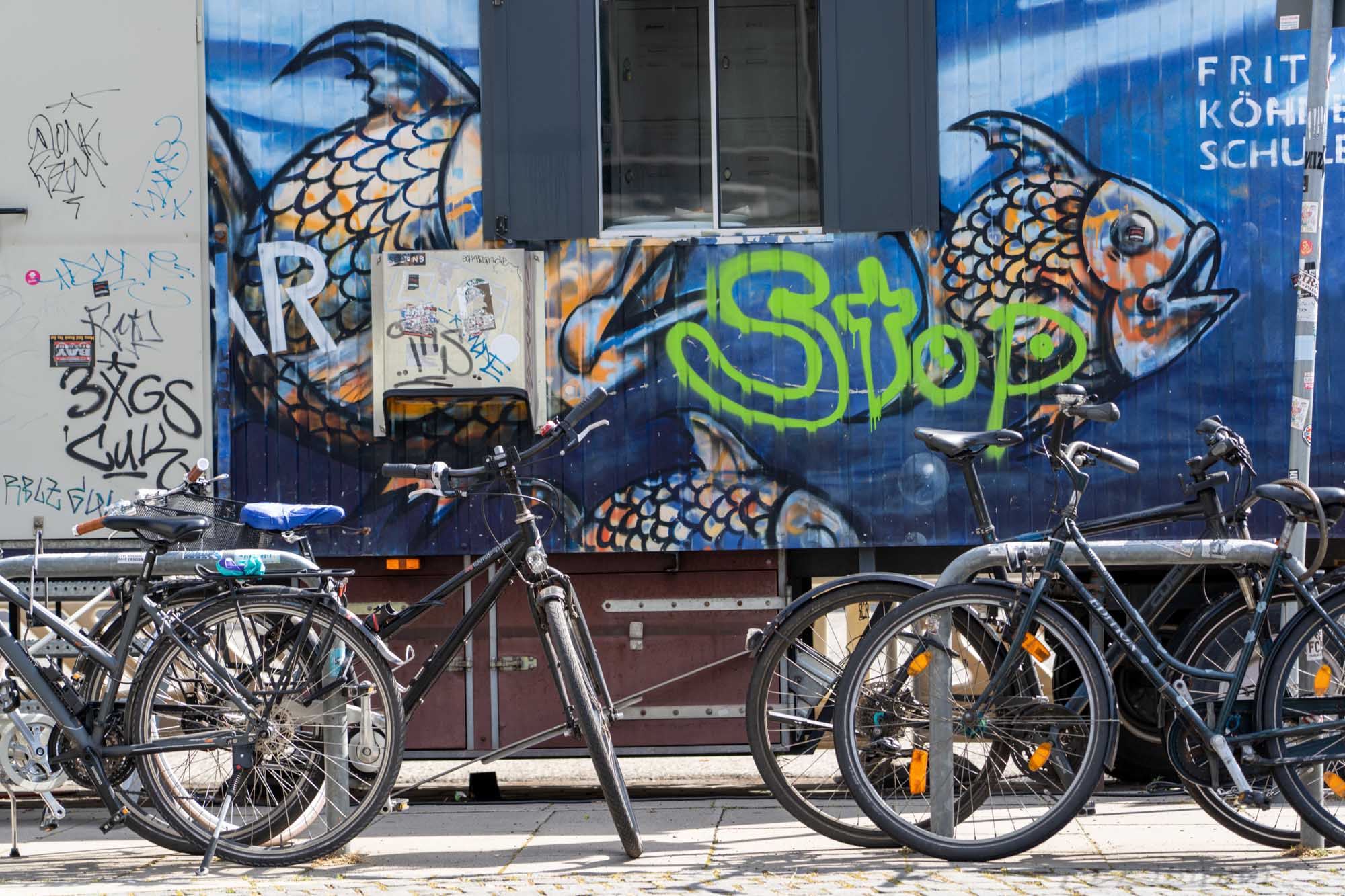 Bicycles parked in front of a graffiti-decorated wall featuring colorful fish and the word Stop in green.