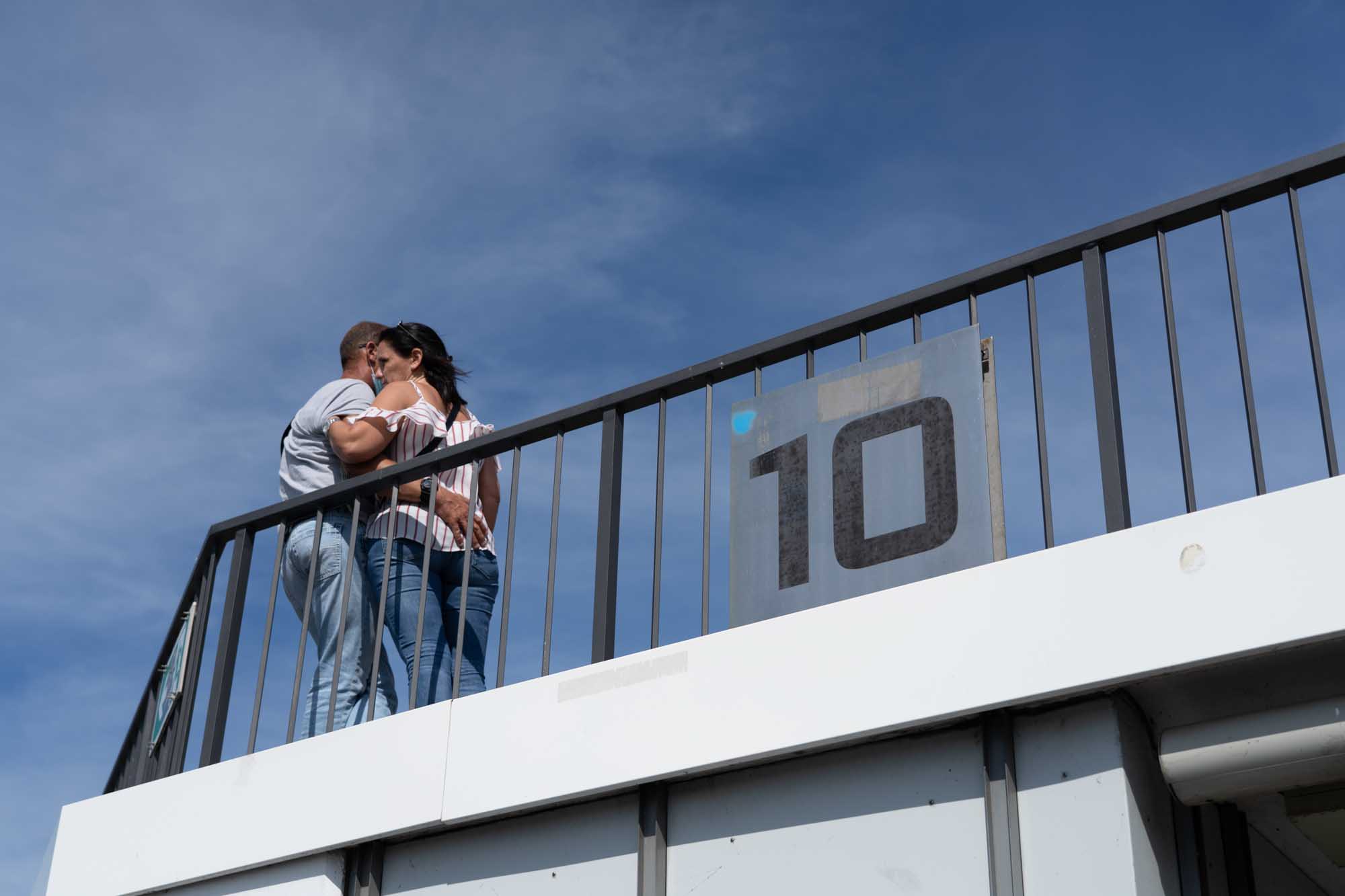 Couple embracing on a balcony with a large 10 sign under a clear blue sky.