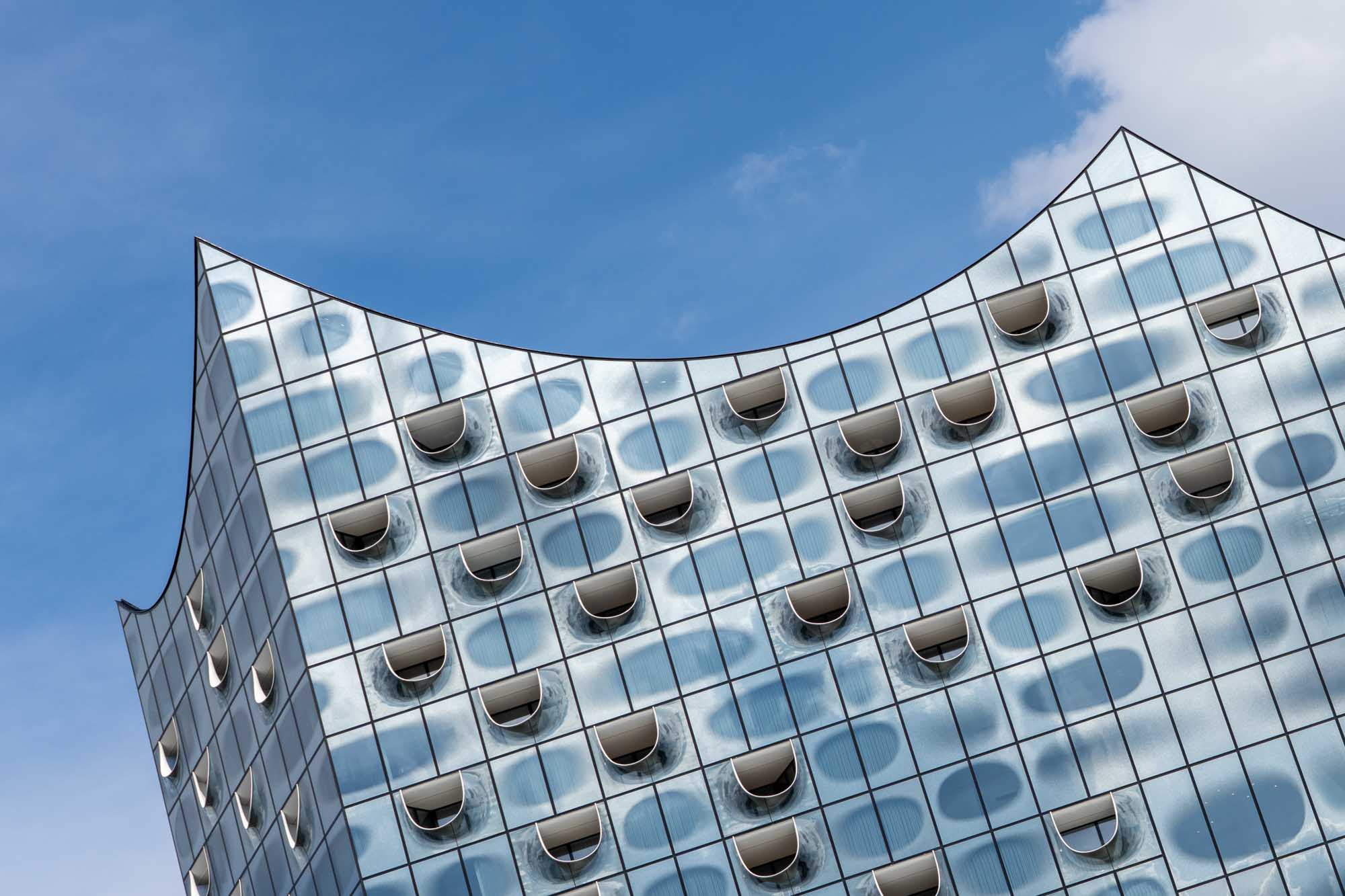 Modern building with curved glass facade and unique window designs against a clear blue sky.