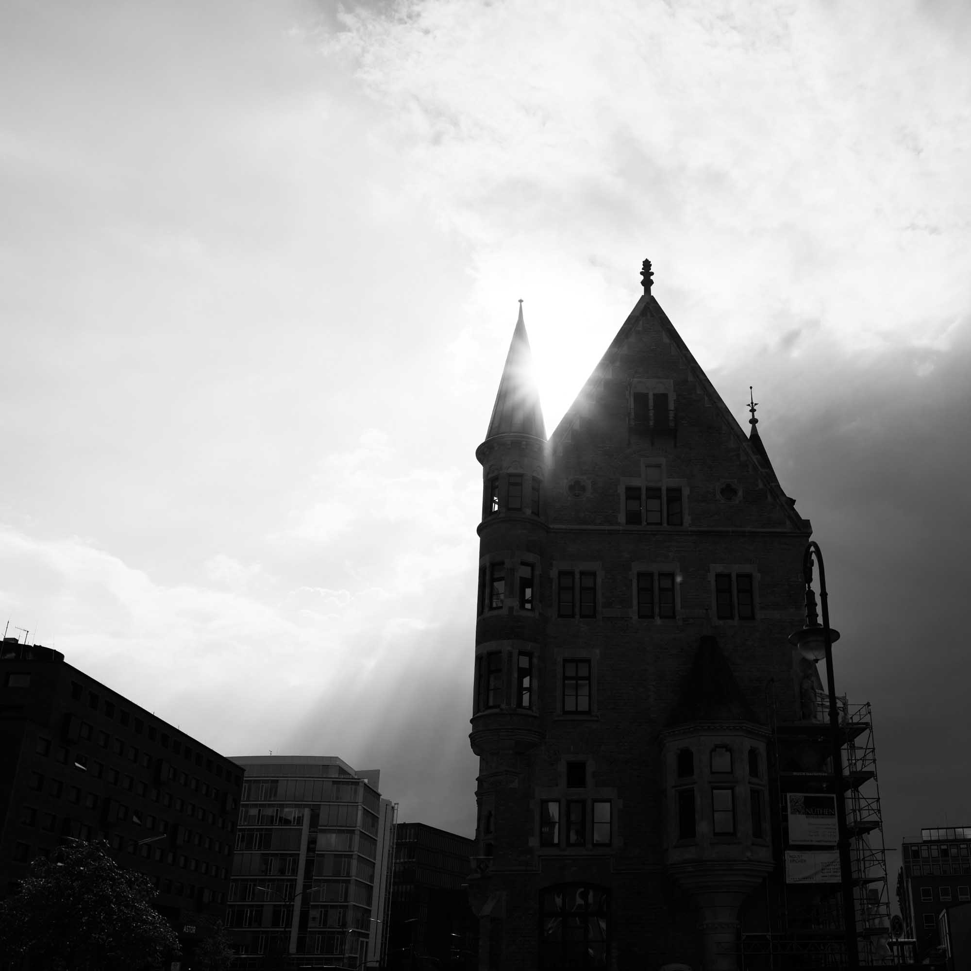Historic Gothic building silhouette with sunlight peeking through towers, contrasted against a dramatic sky.
