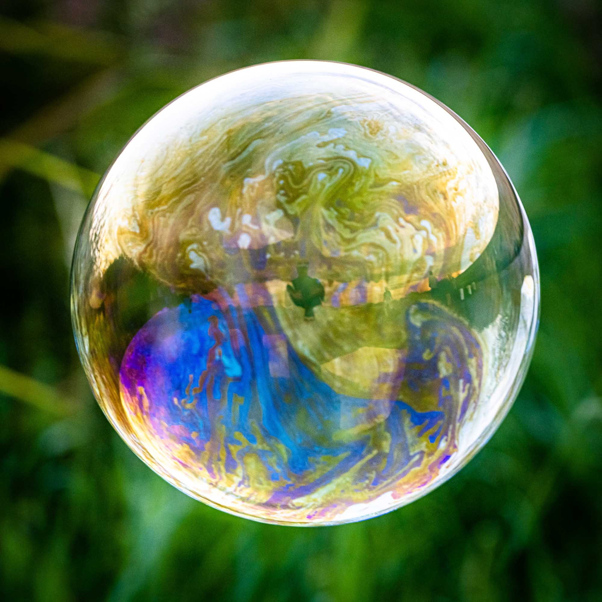 Colorful soap bubble with swirling patterns against a blurred green background.