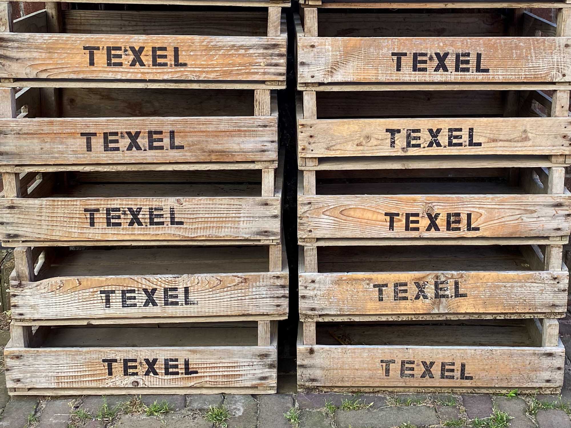 Wooden crates labeled TEXEL stacked on a paved surface outdoors.
