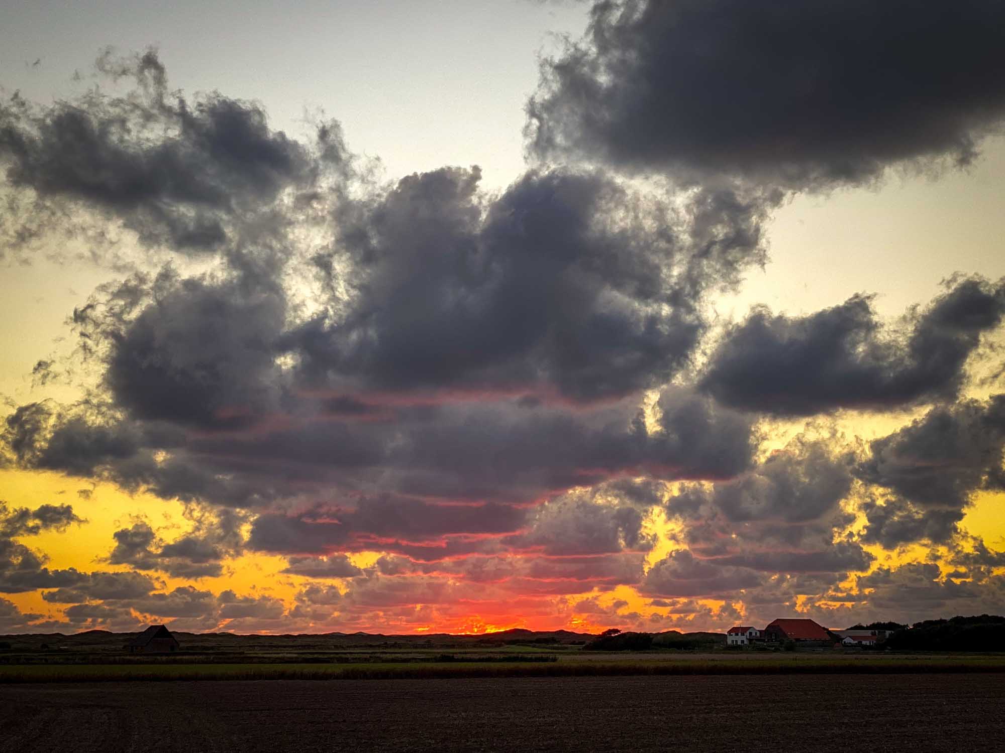 Vibrant sunset over a rural landscape with clouds and houses silhouetted against the colorful sky.