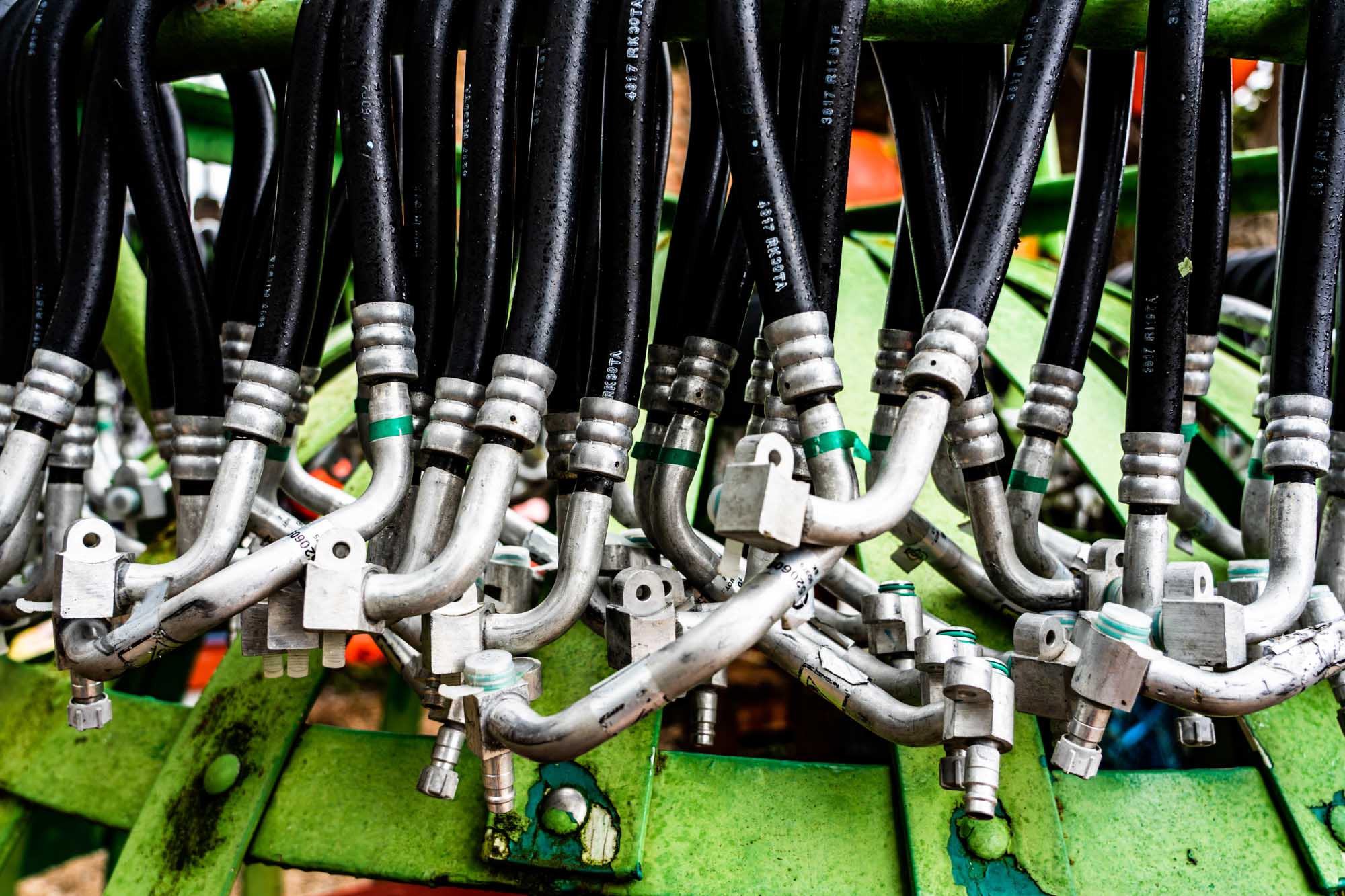 Close-up of industrial hydraulic hoses and metal fittings on green machinery.