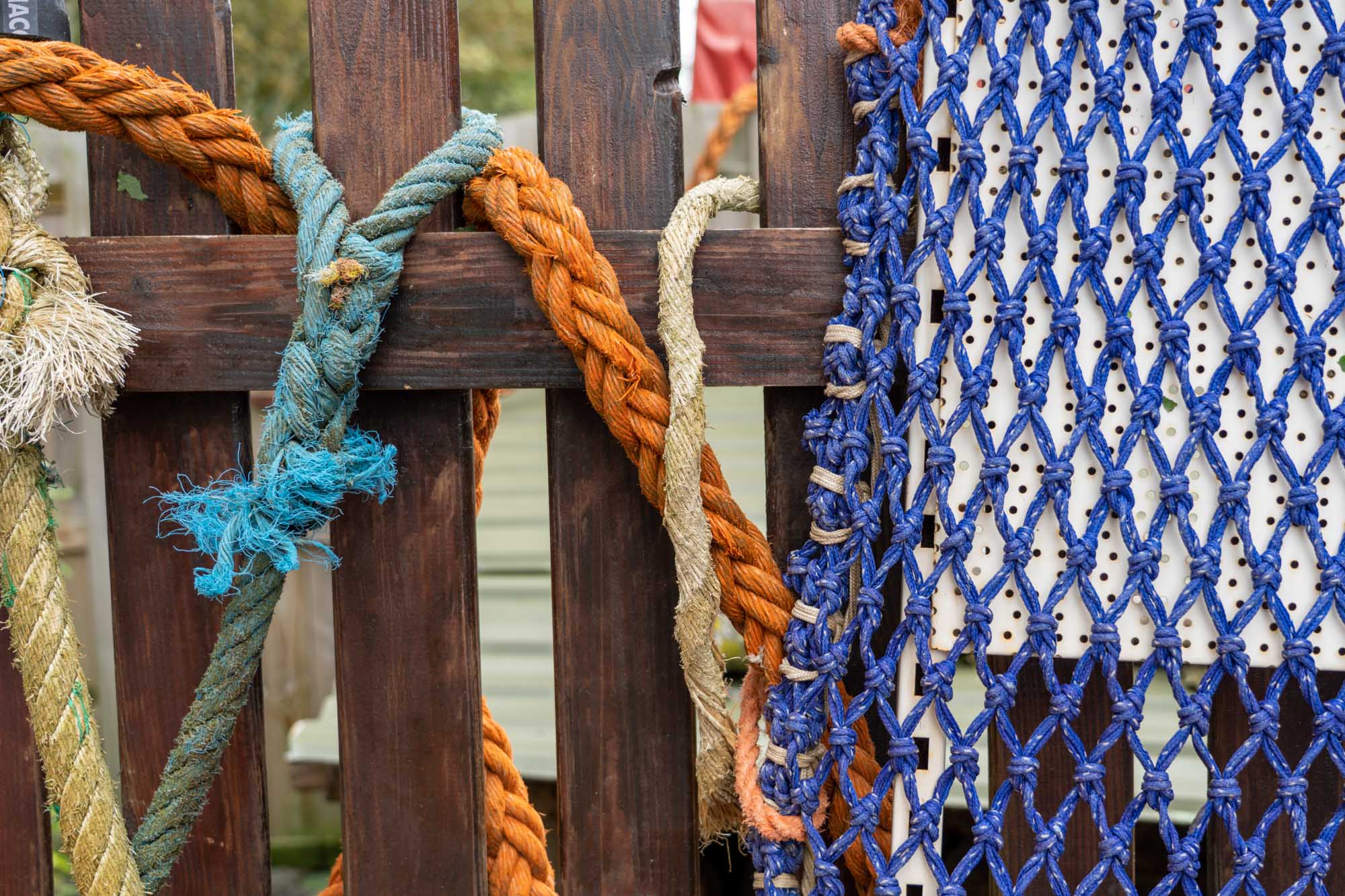 Close-up of colorful ropes and a blue net draped over a wooden fence.