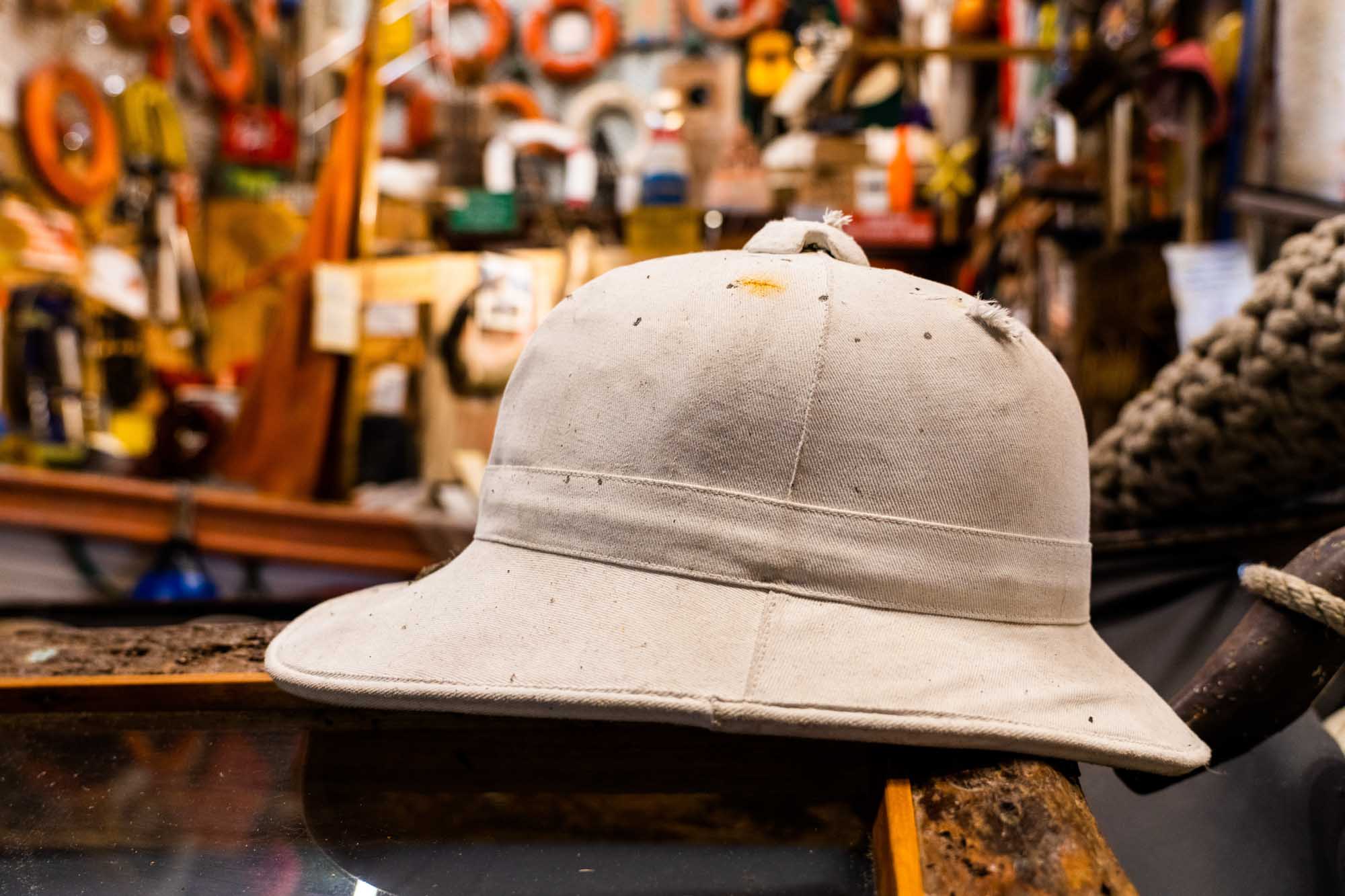 Vintage safari helmet on rustic table in cluttered workshop with nautical gear and colorful ropes in background.