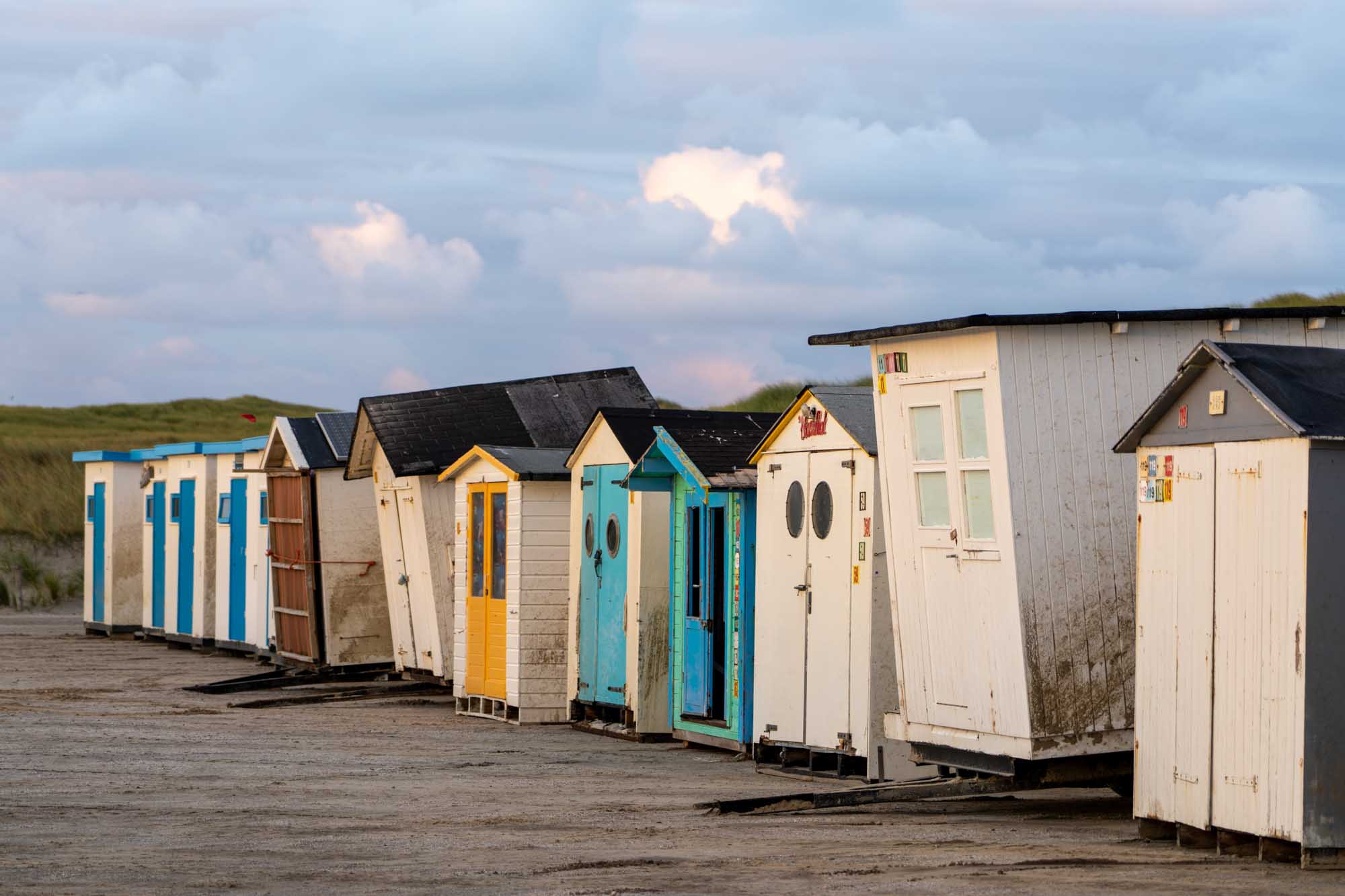 Colorful beach huts lined up under a cloudy sky on a sandy coast.
