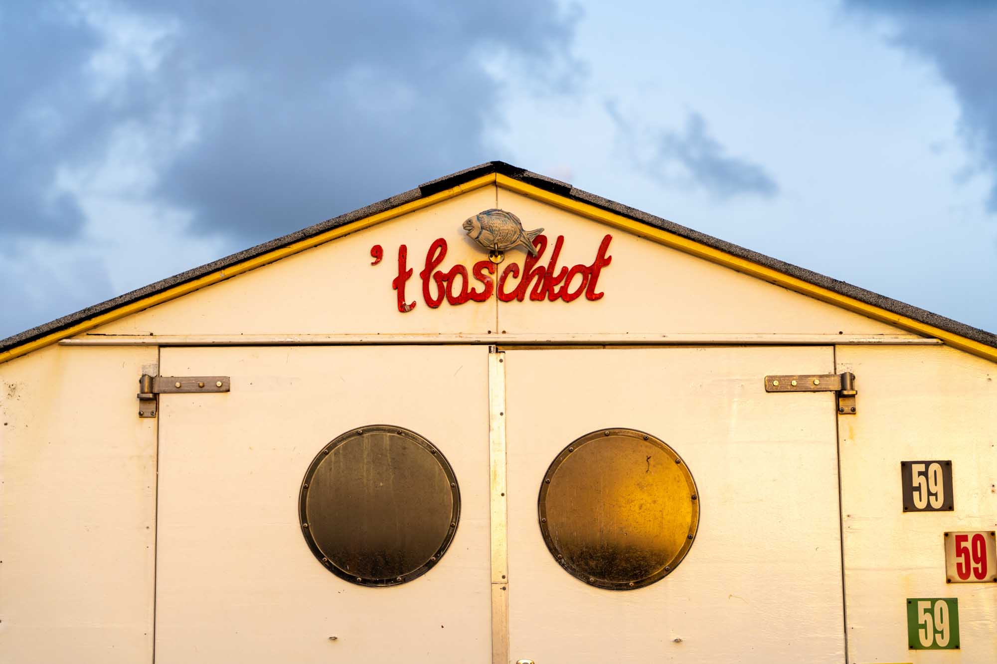 Beach shack with circular windows, t, baschkot sign in red, cloudy sky. Number 59 displayed on the side.