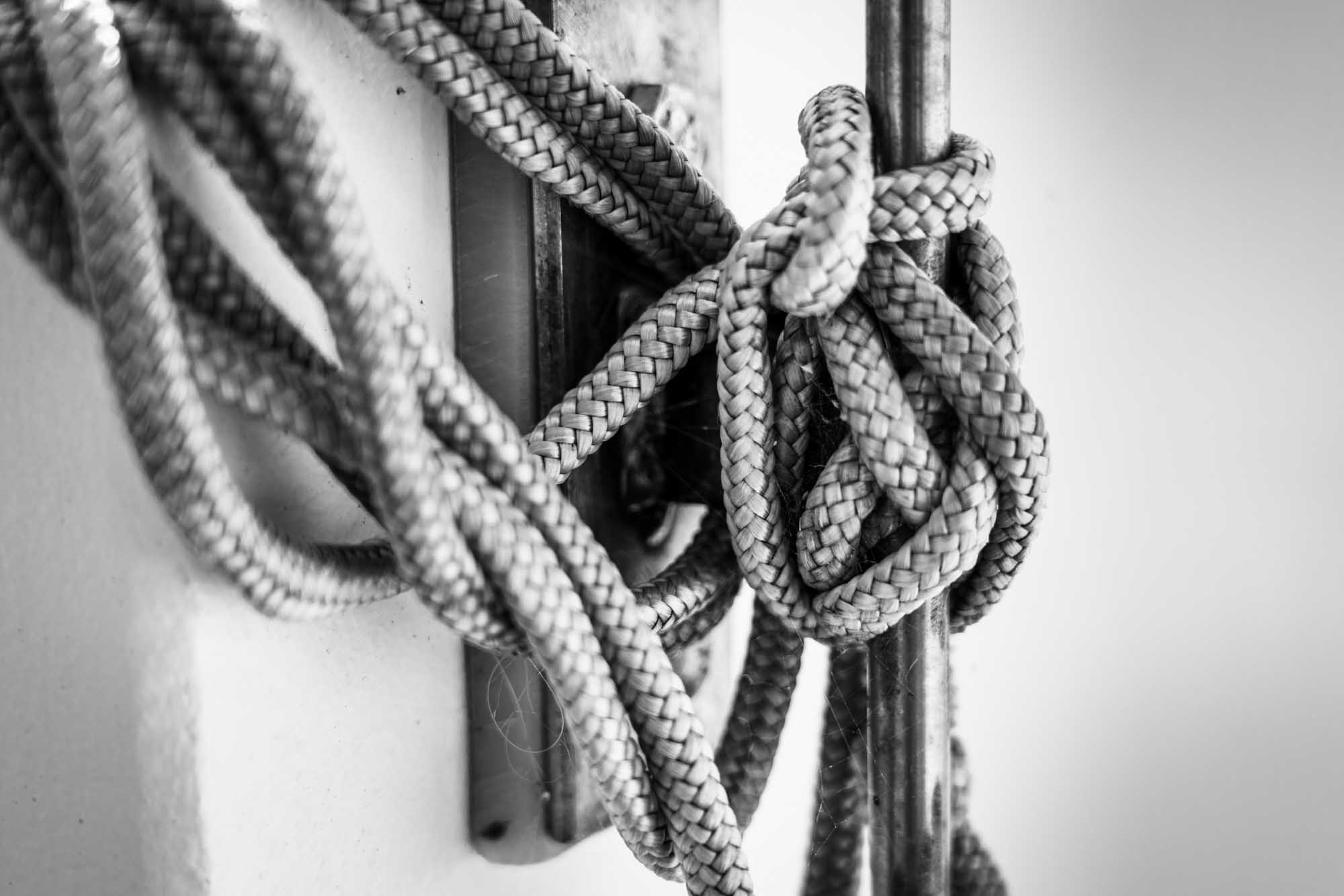 Close-up of a braided rope tied in a complex knot around metal poles, in black and white.