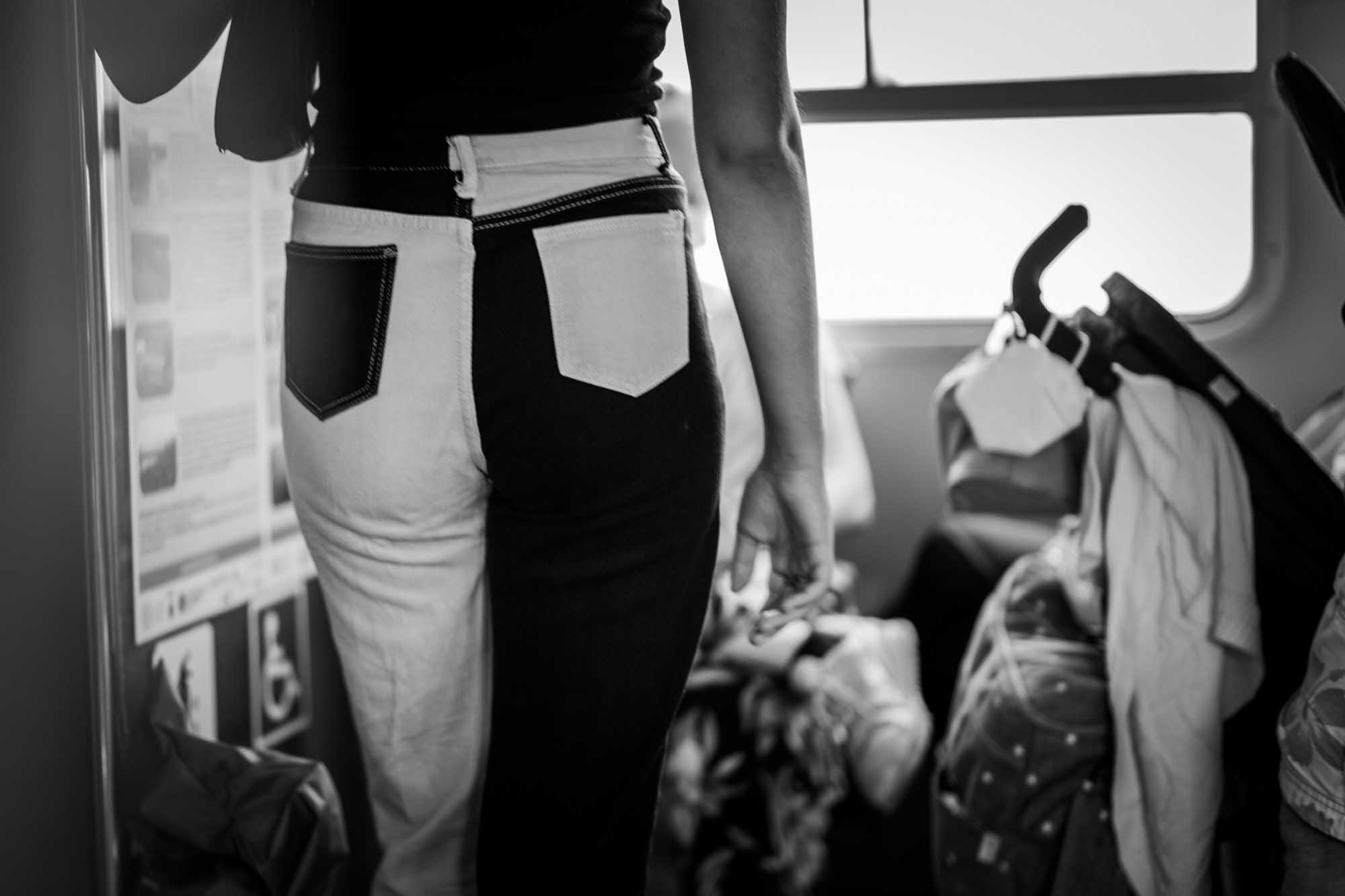 Black and white photo of a person in two-toned jeans standing inside a vehicle, with bags and stroller nearby.