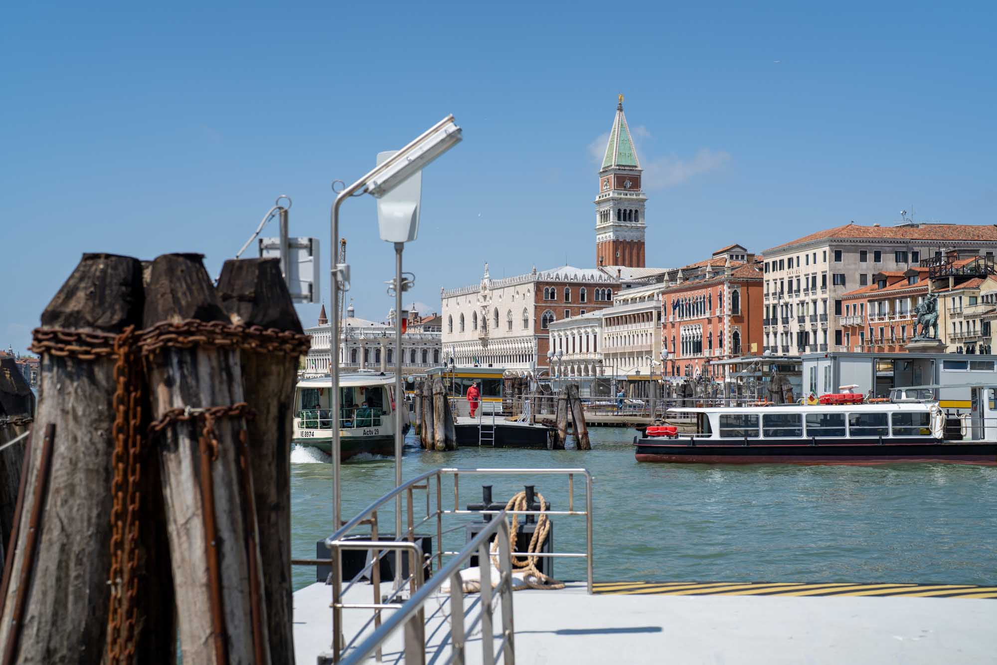 Venice canal scene with boats, historic buildings, and St. Mark's Campanile under a clear blue sky.