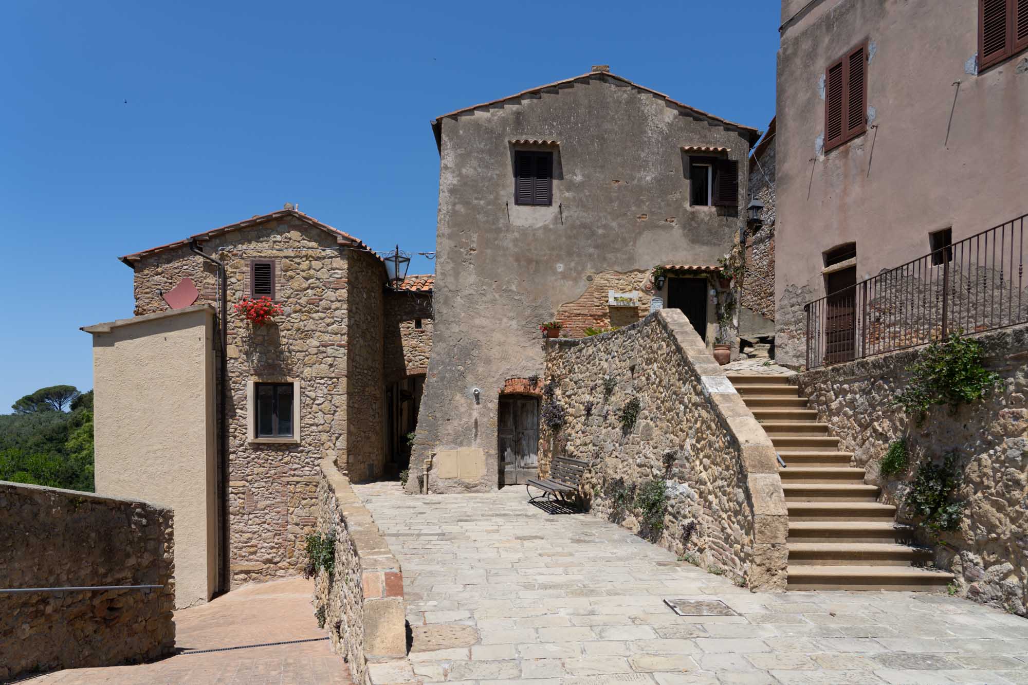 Charming old stone buildings with stairs and a vibrant red flower pot under a clear blue sky.