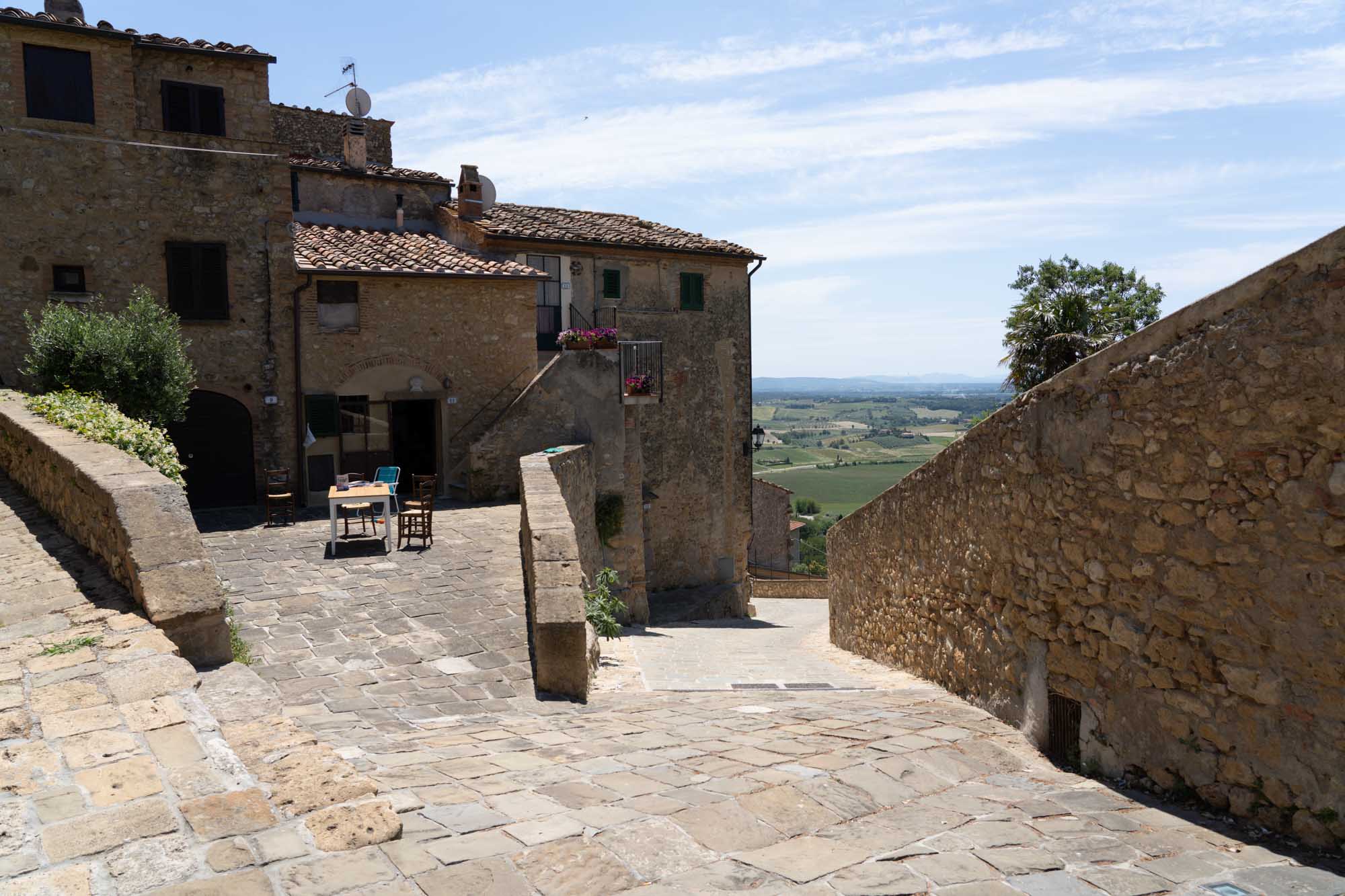 Historic stone courtyard with outdoor seating overlooking a scenic countryside vista under a blue sky.
