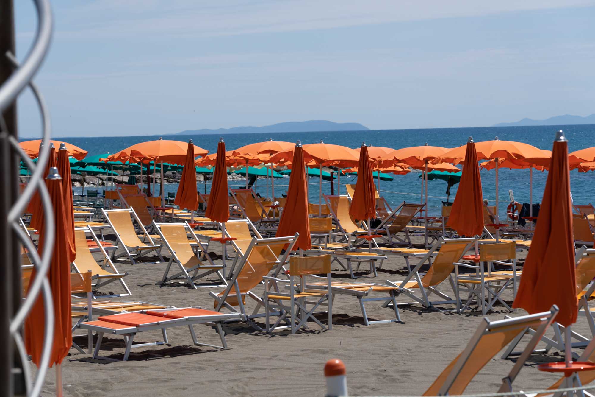 Orange beach umbrellas and sun loungers on a sandy beach with a calm sea in the background.