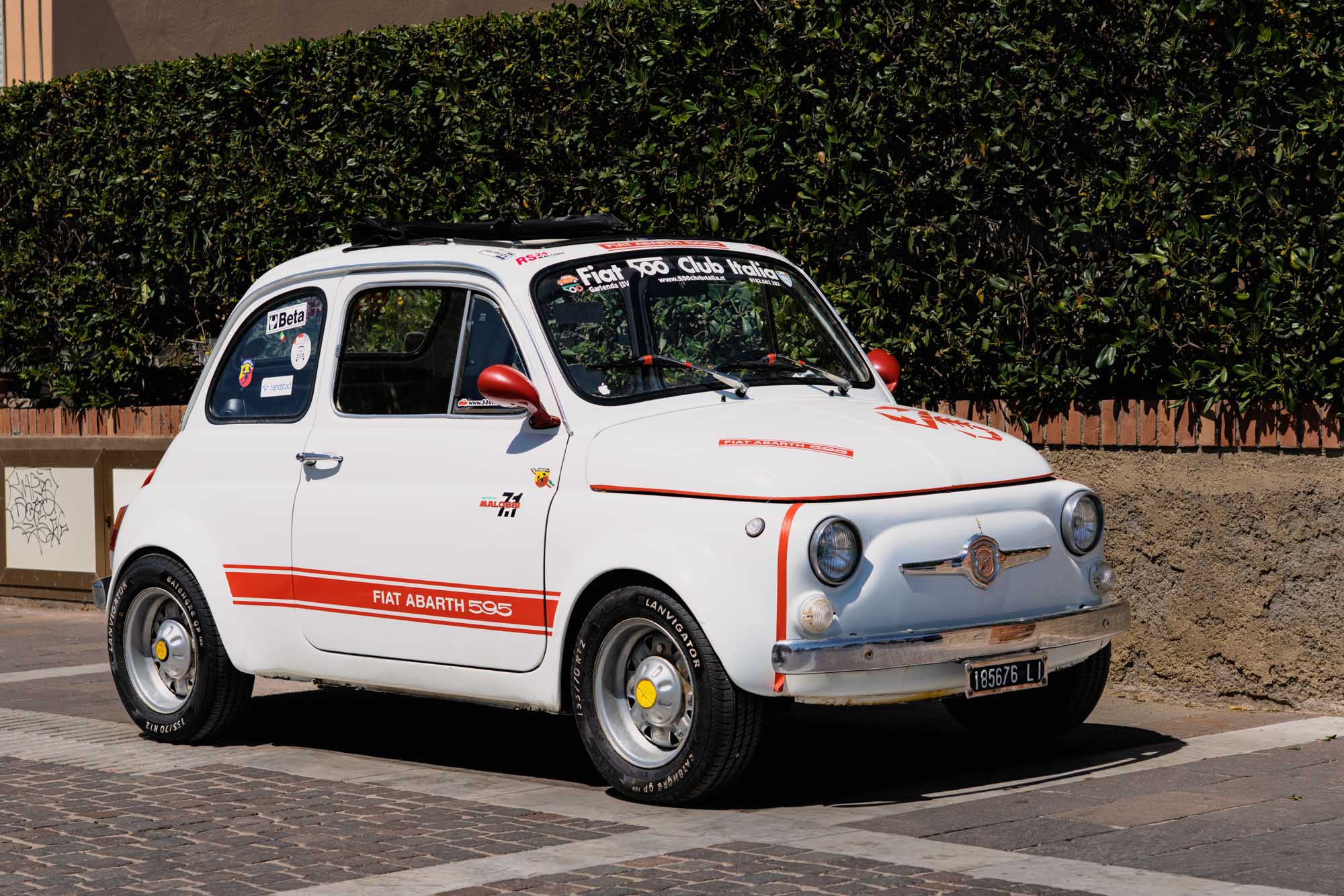 Vintage white Fiat Abarth 595 parked on a street, showcasing classic car design with red trim and decals.