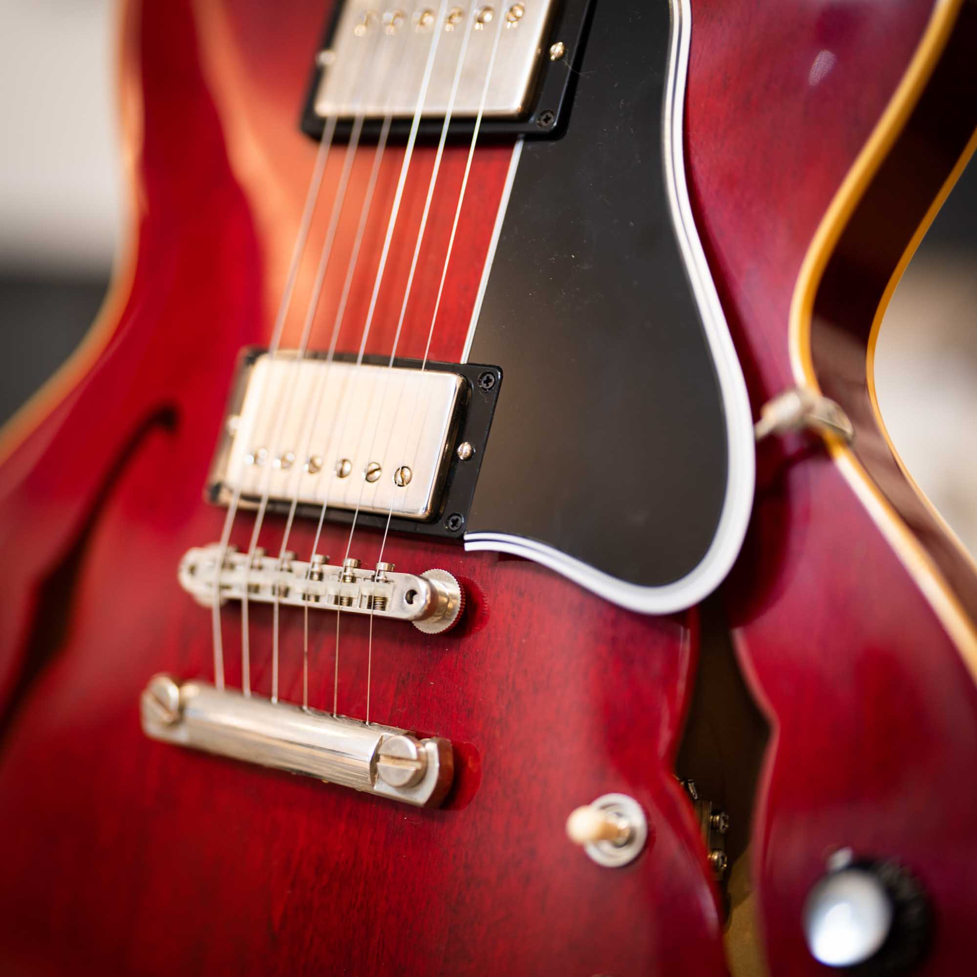 Close-up of a red electric guitar body with strings, pickups, and black pickguard.