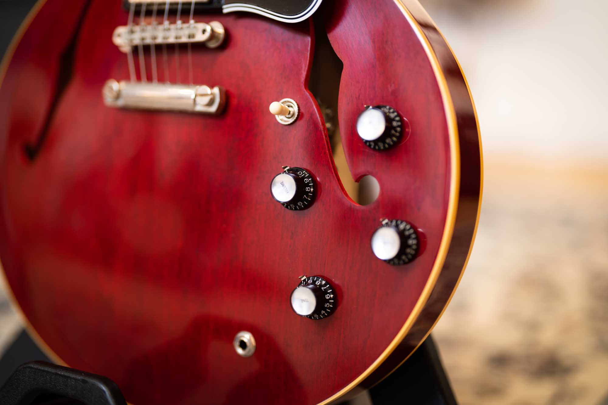 Close-up of a red semi-hollow electric guitar on a stand, showing its knobs and strings.
