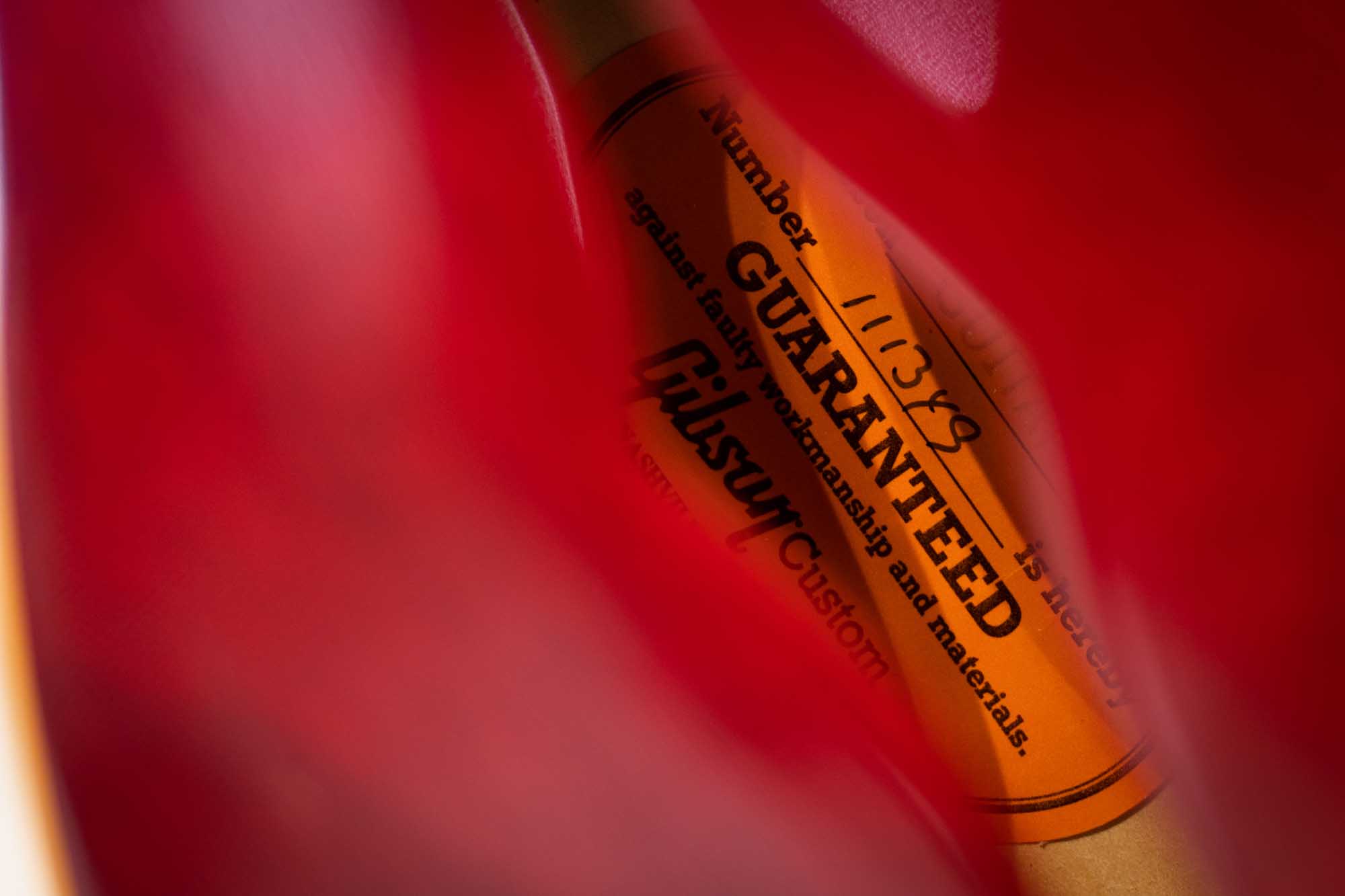 Close-up of a red guitar interior label with a warranty guarantee and serial number visible.
