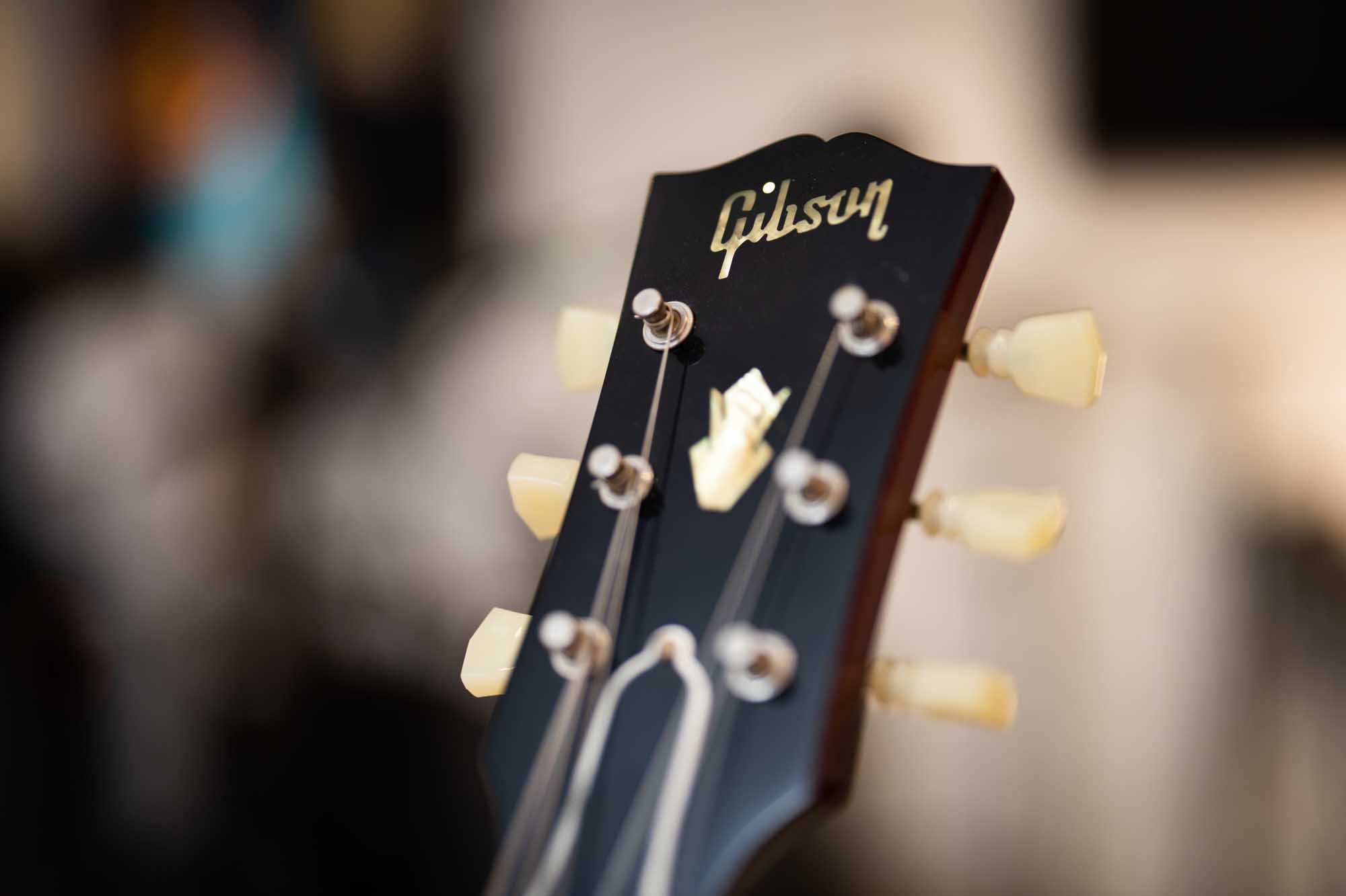 Close-up of a black Gibson guitar headstock with tuning pegs, blurred background.