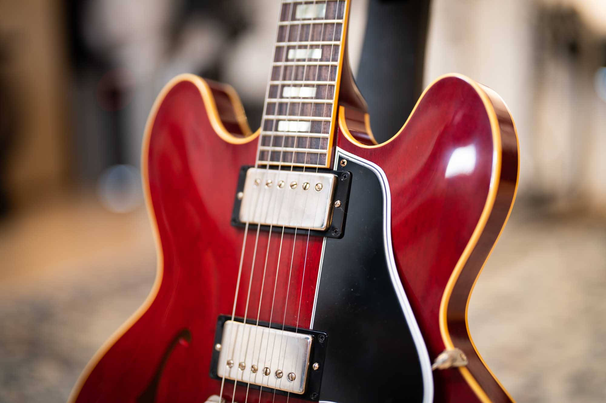 Red semi-hollow electric guitar with chrome pickups and black pickguard, showcasing a rich wood finish and strings.