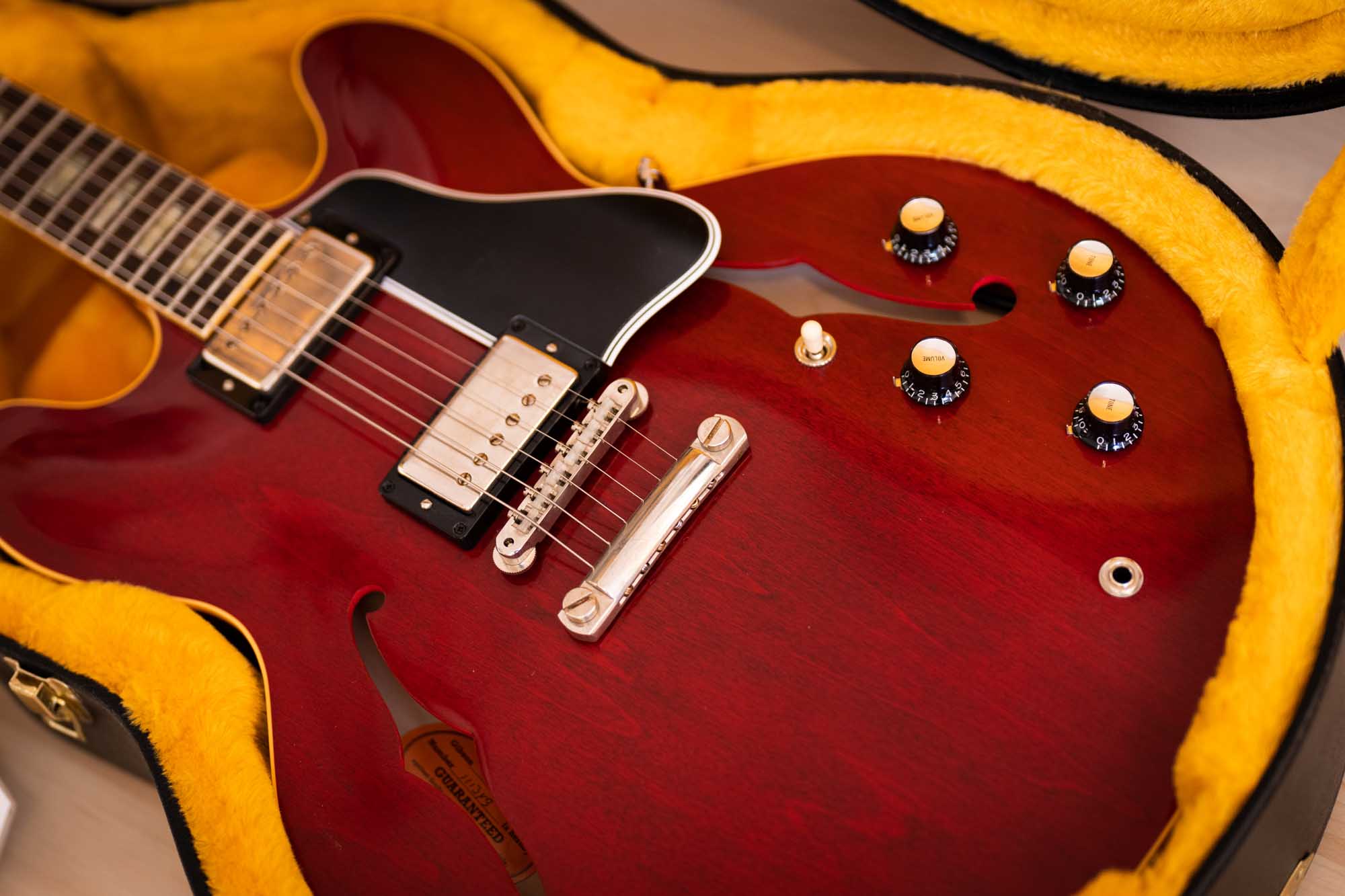 Red semi-hollow electric guitar in plush yellow-lined case, showcasing controls and bridge close-up.