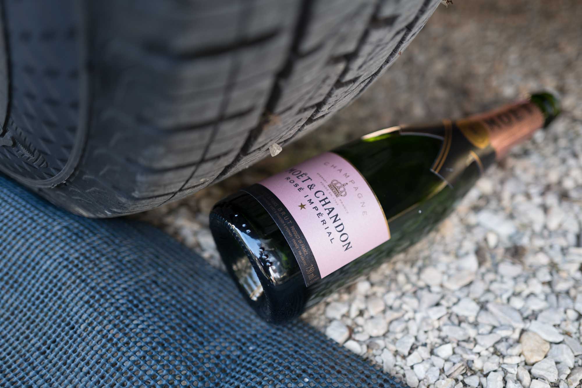Car tire near Moet & Chandon Rosé Impérial champagne bottle on a gravel surface.
