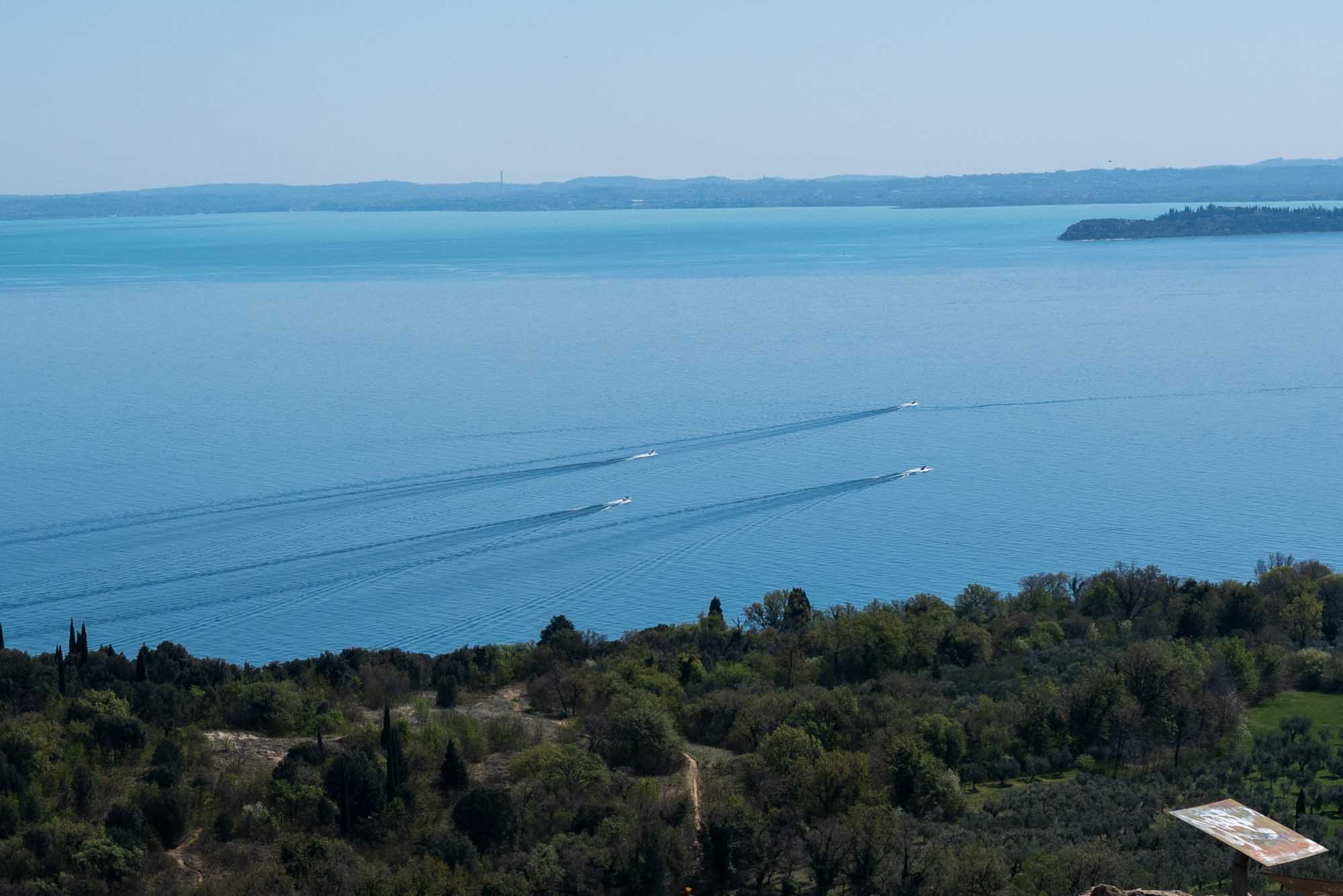 Boats sailing across a serene blue lake with surrounding lush greenery and distant shoreline.