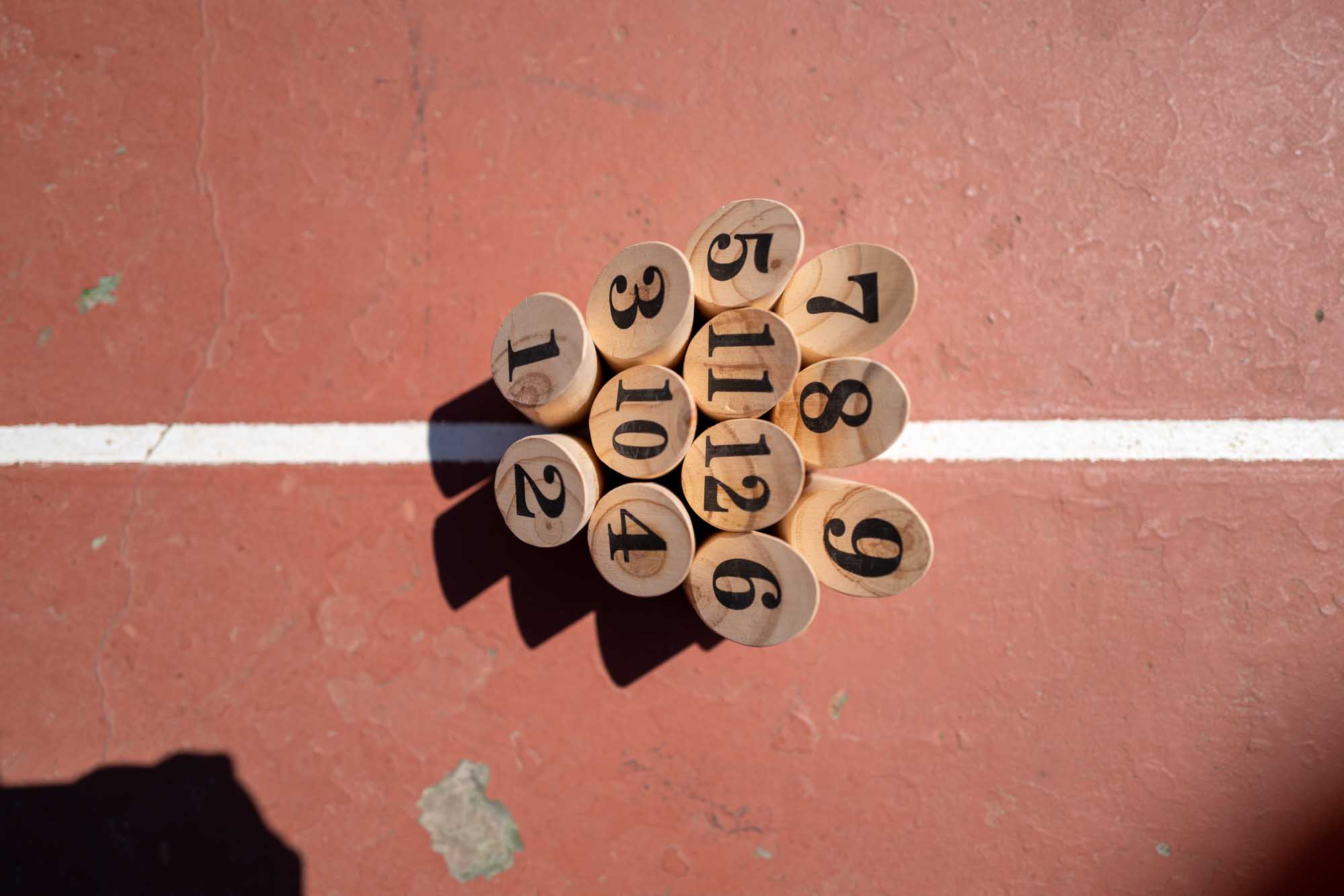 Numbered wooden dowels arranged on a red court surface with a white line crossing.