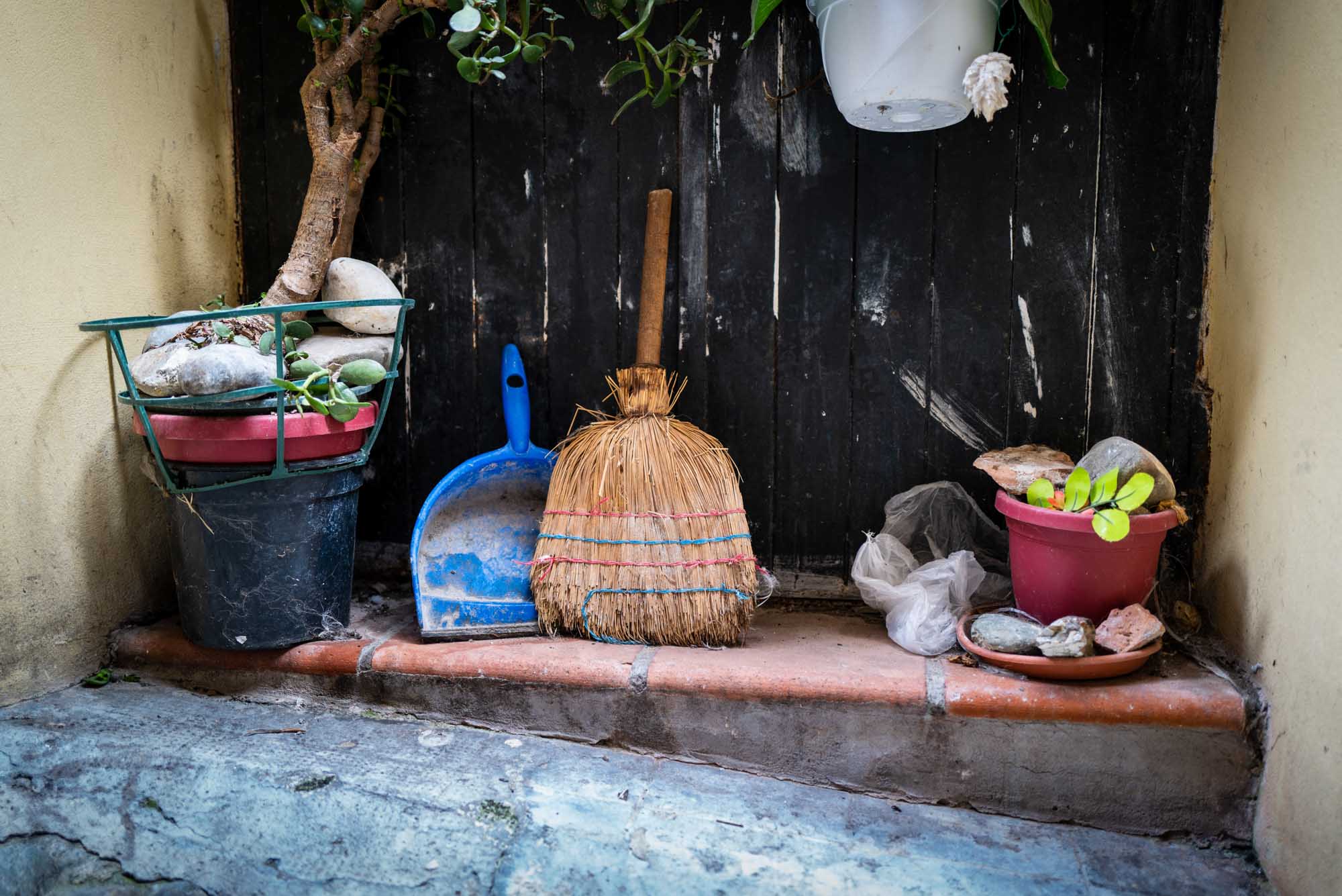 Broom, dustpan, and potted plants with rocks on a step against a black wooden wall.