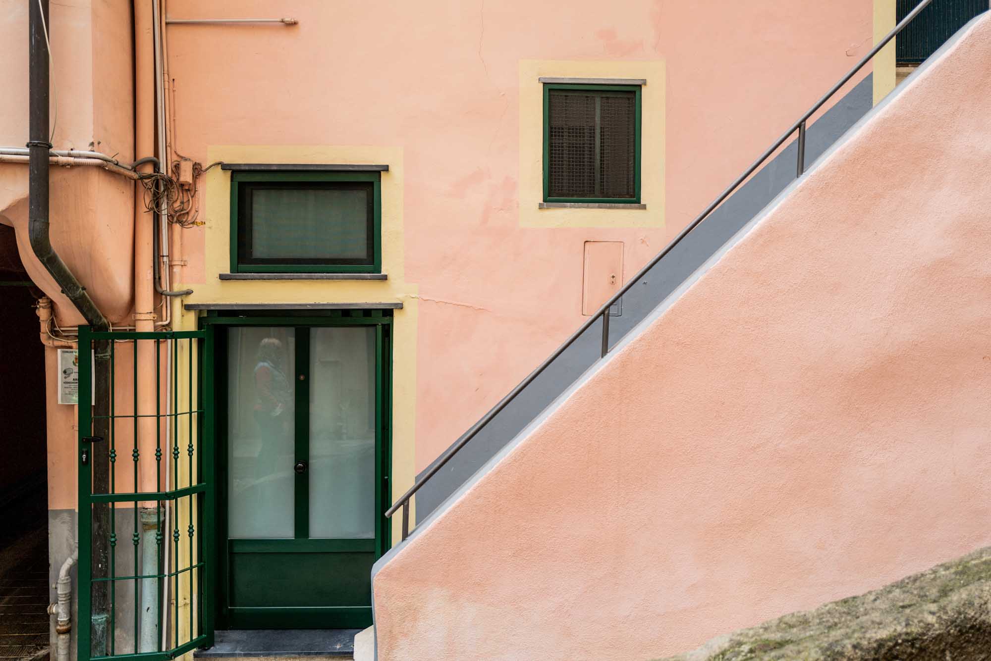 Peach stucco wall with a green door, window, and diagonal staircase railing in an urban setting.