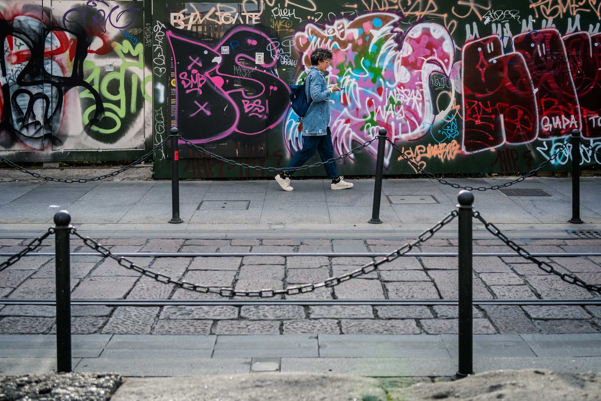 Person walking past graffiti-covered wall in urban setting.
