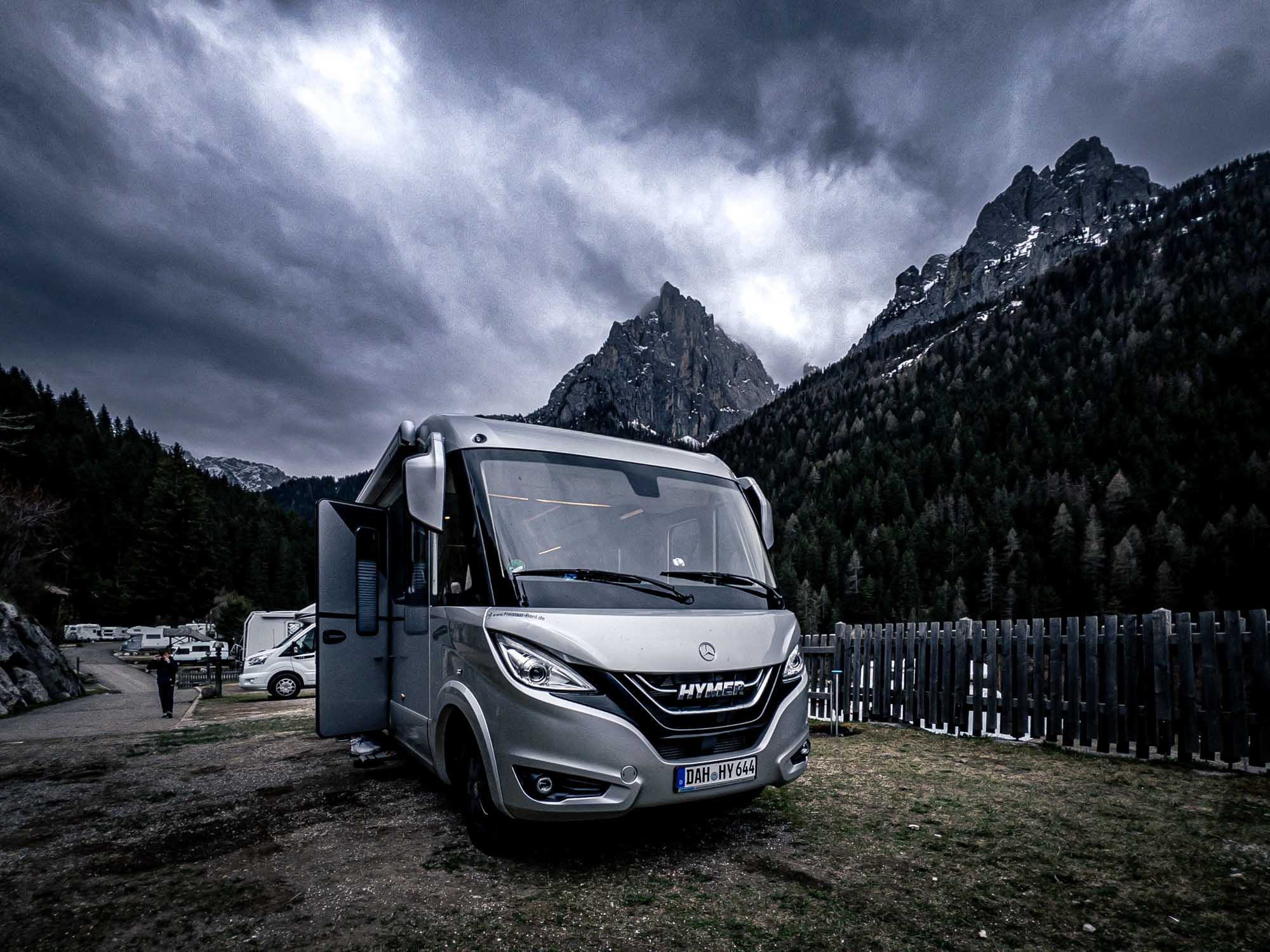 Luxury RV parked in scenic mountain campsite with towering peaks and cloudy sky in the background.