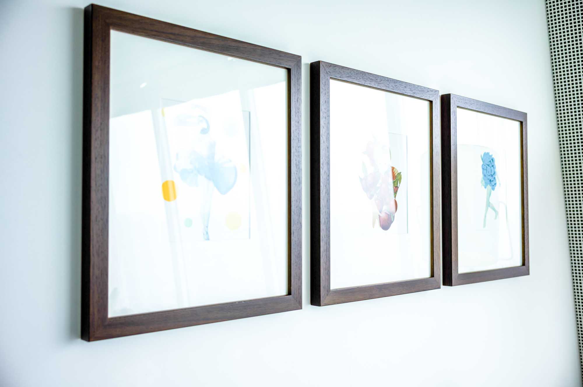 Three framed minimalist artworks on a white wall with floral and abstract designs, in a modern interior setting.