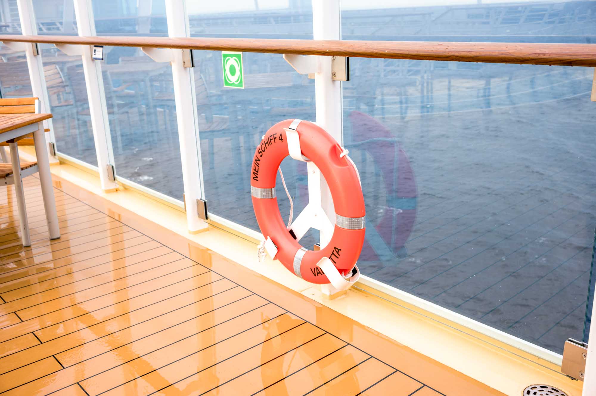 Orange life buoy on ship deck with glass railing overlooking the sea, labeled MEIN SCHIFF 4.