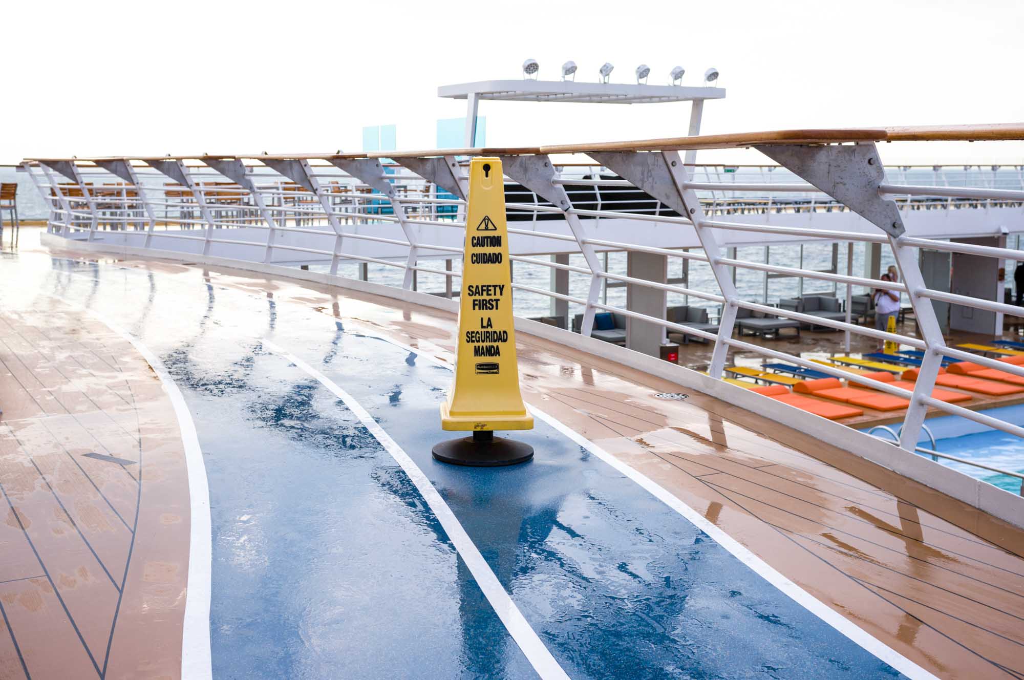 Wet cruise ship deck with caution cone and poolside chairs.