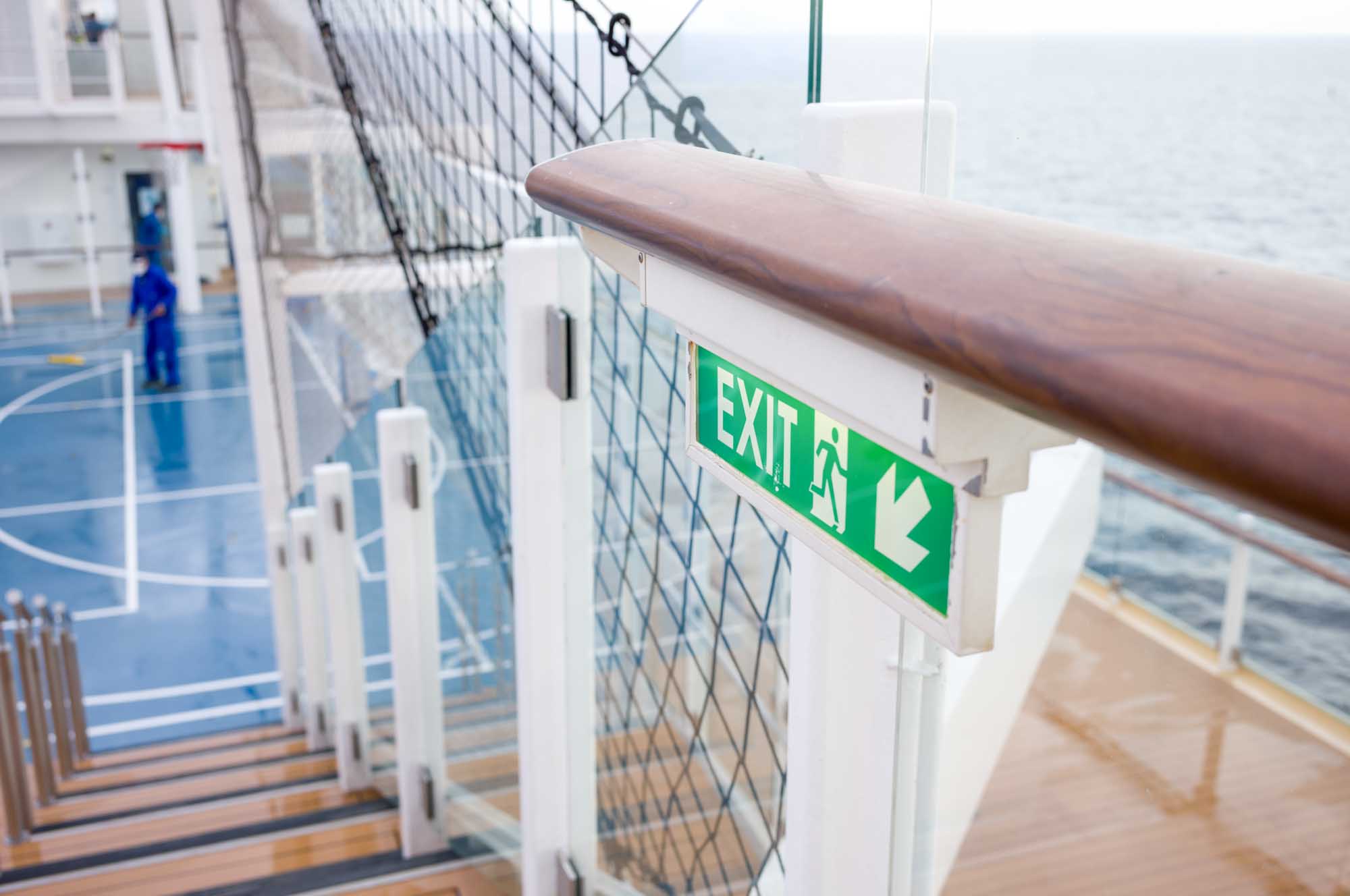 Green exit sign near ship stairway leading to deck, overlooking ocean background.