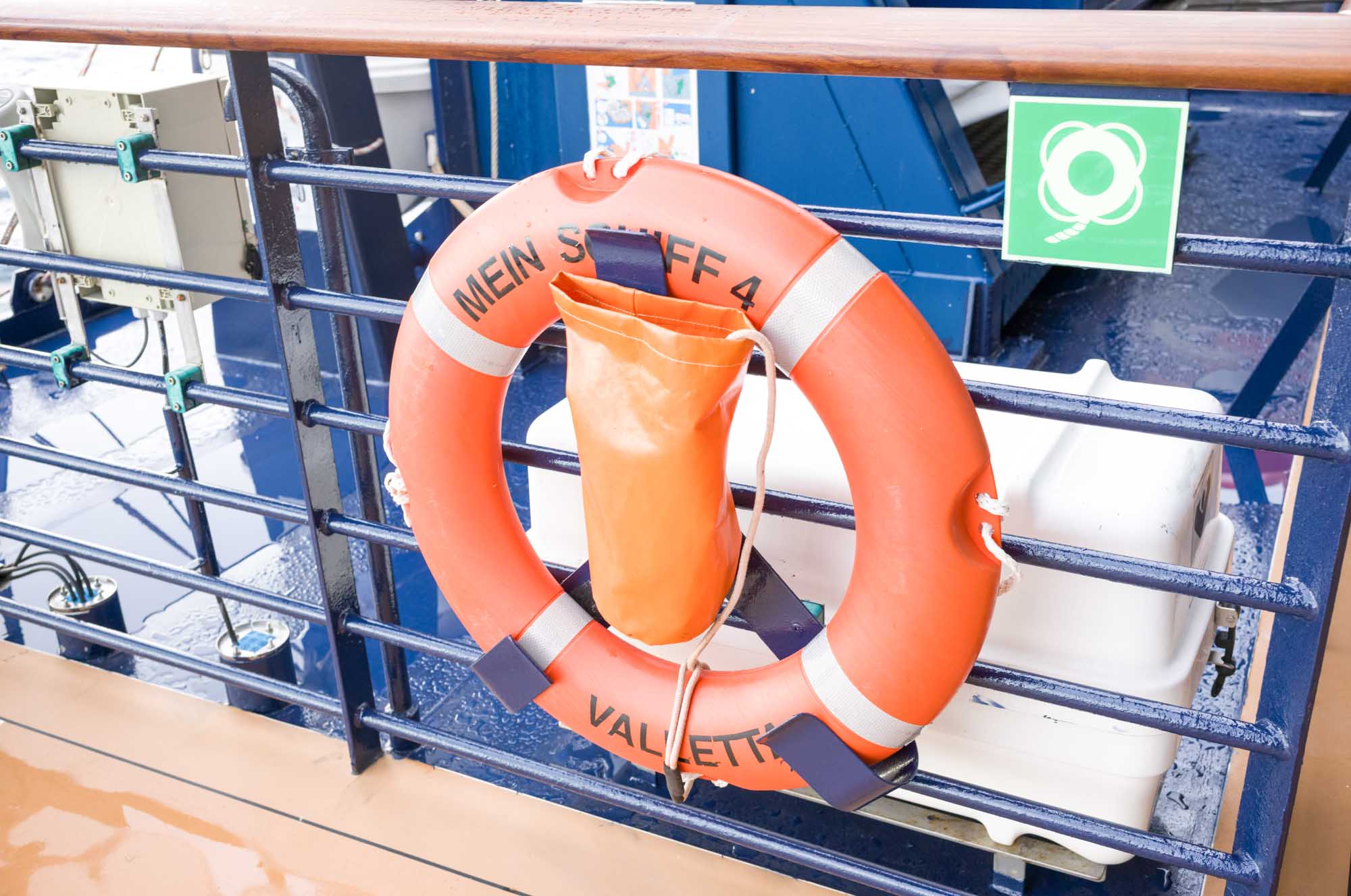 Orange lifebuoy with Mein Schiff 4 text attached to a ship's metal rail, safety equipment visible.