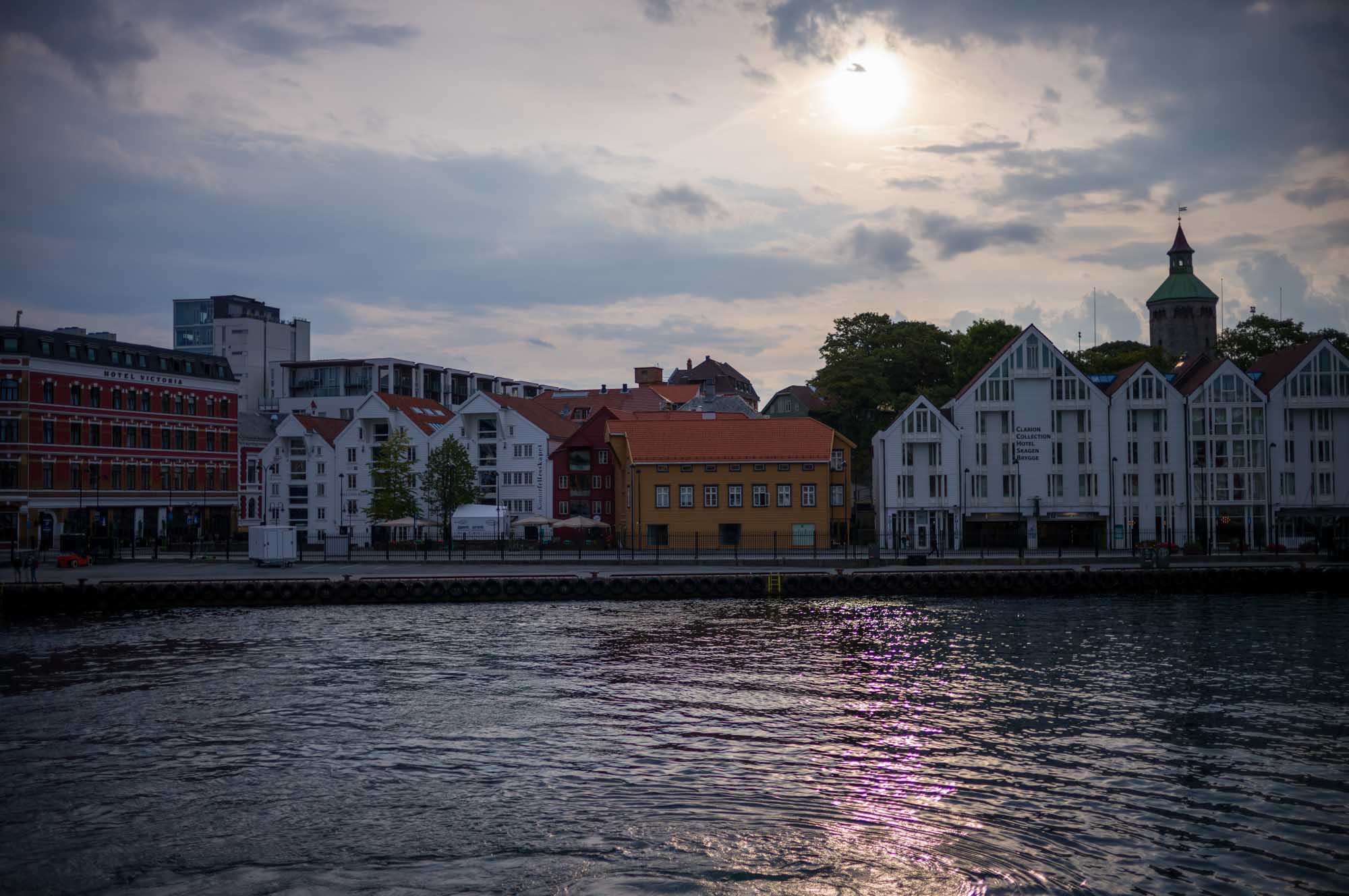 Waterfront view of colorful buildings and cloudy sky reflecting in water at sunset.