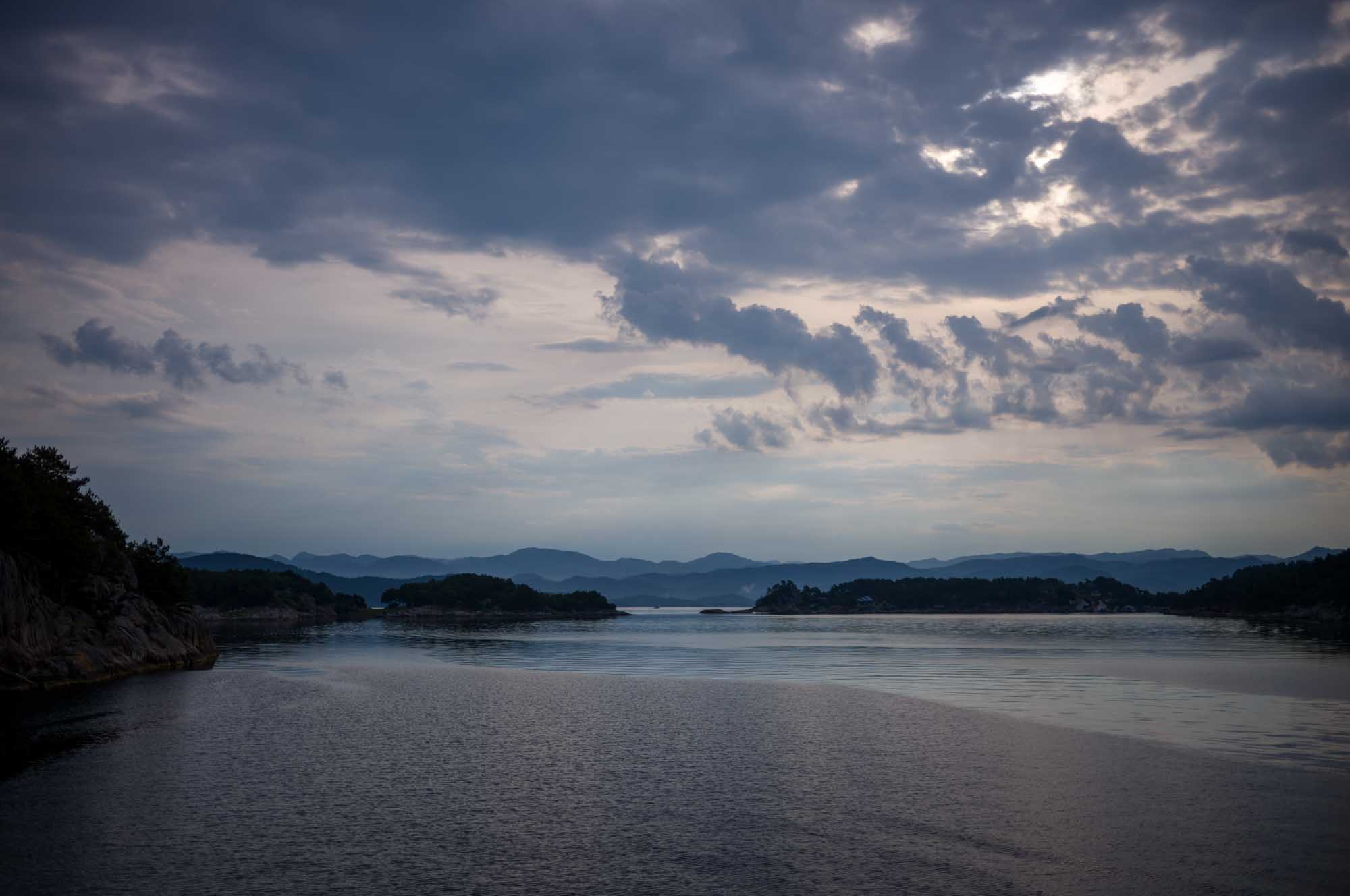 Tranquil seascape with cloudy sky over calm water and distant hills in the evening.
