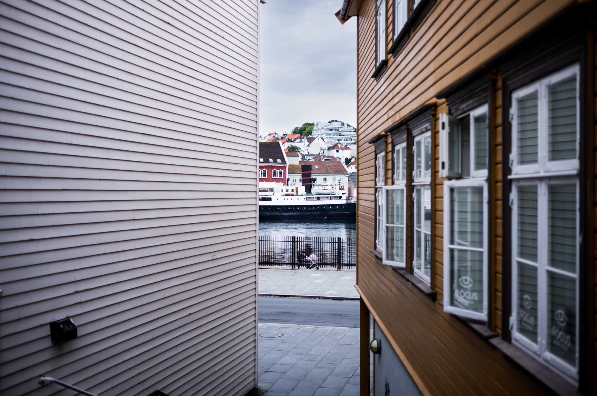 Narrow alley view of harbor with colorful buildings and moored ship in coastal town.