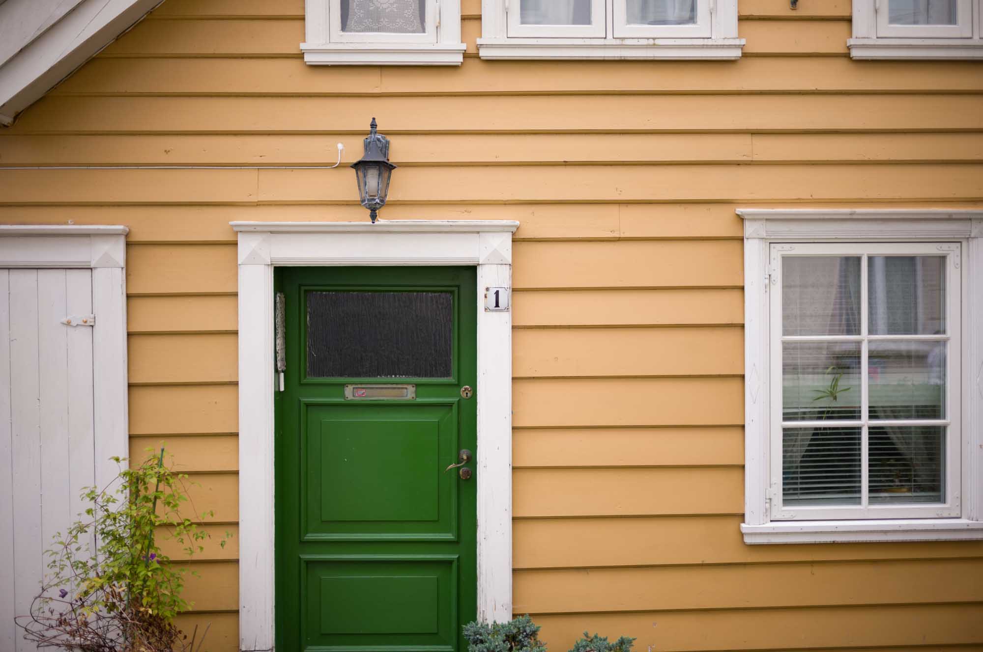 Yellow house exterior with a green door, white-framed windows, and wall lantern, creating a charming residential look.