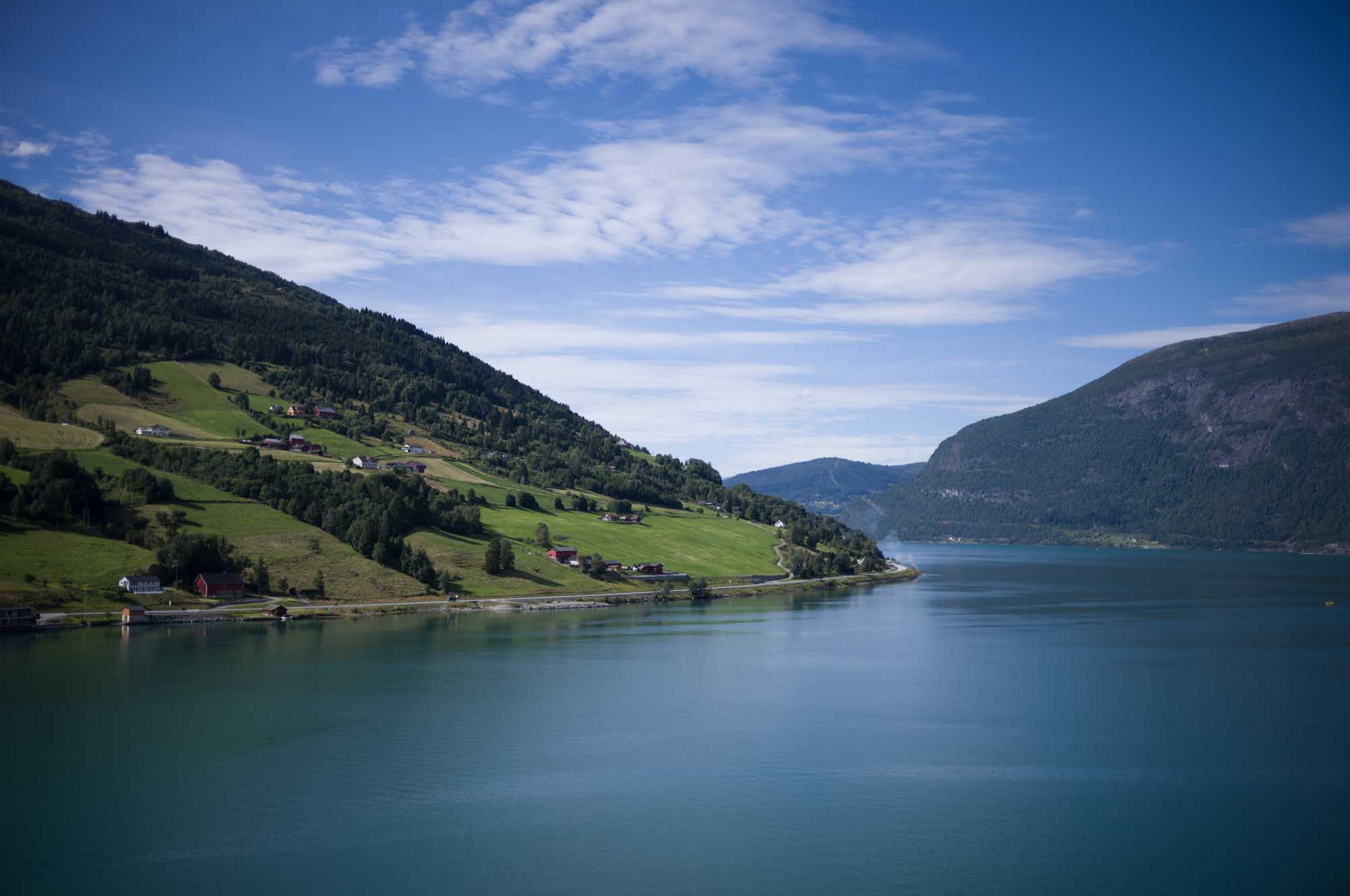 Scenic view of a fjord with green hills, scattered houses, and blue sky in Norway.